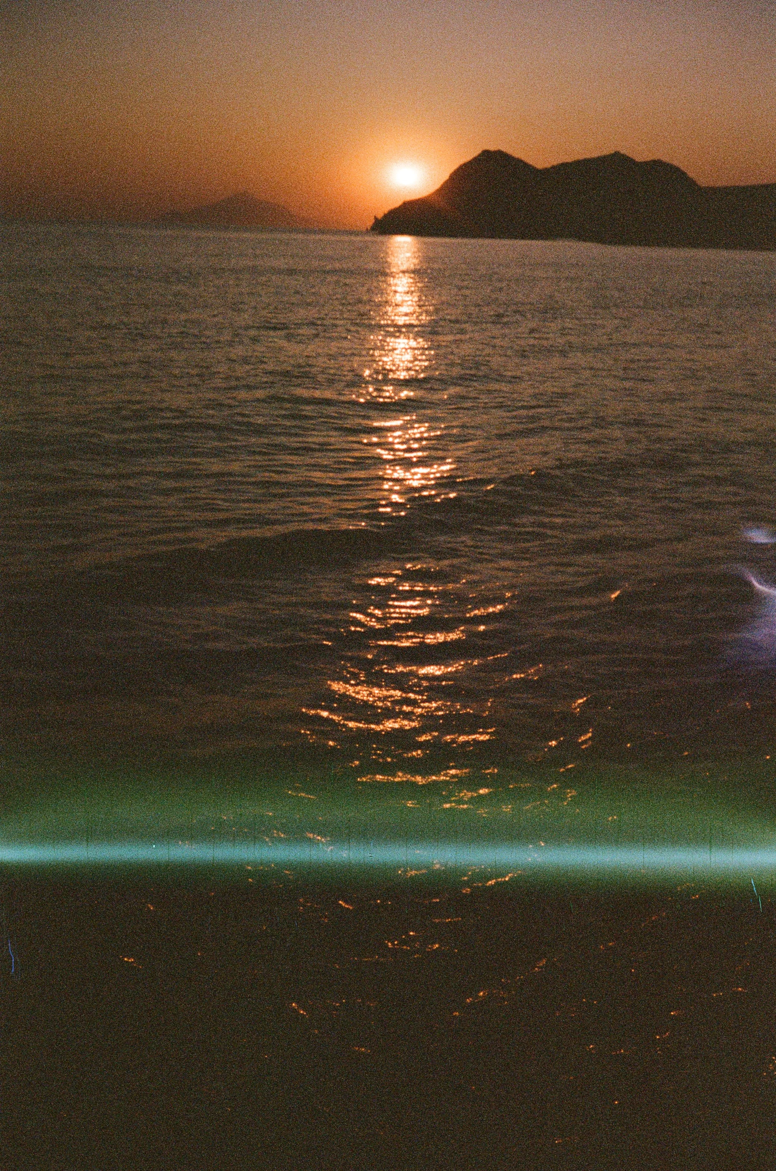 Coucher de soleil sur la mer avec des monts en arrière-plan et la reflection du soleil sur l'eau.