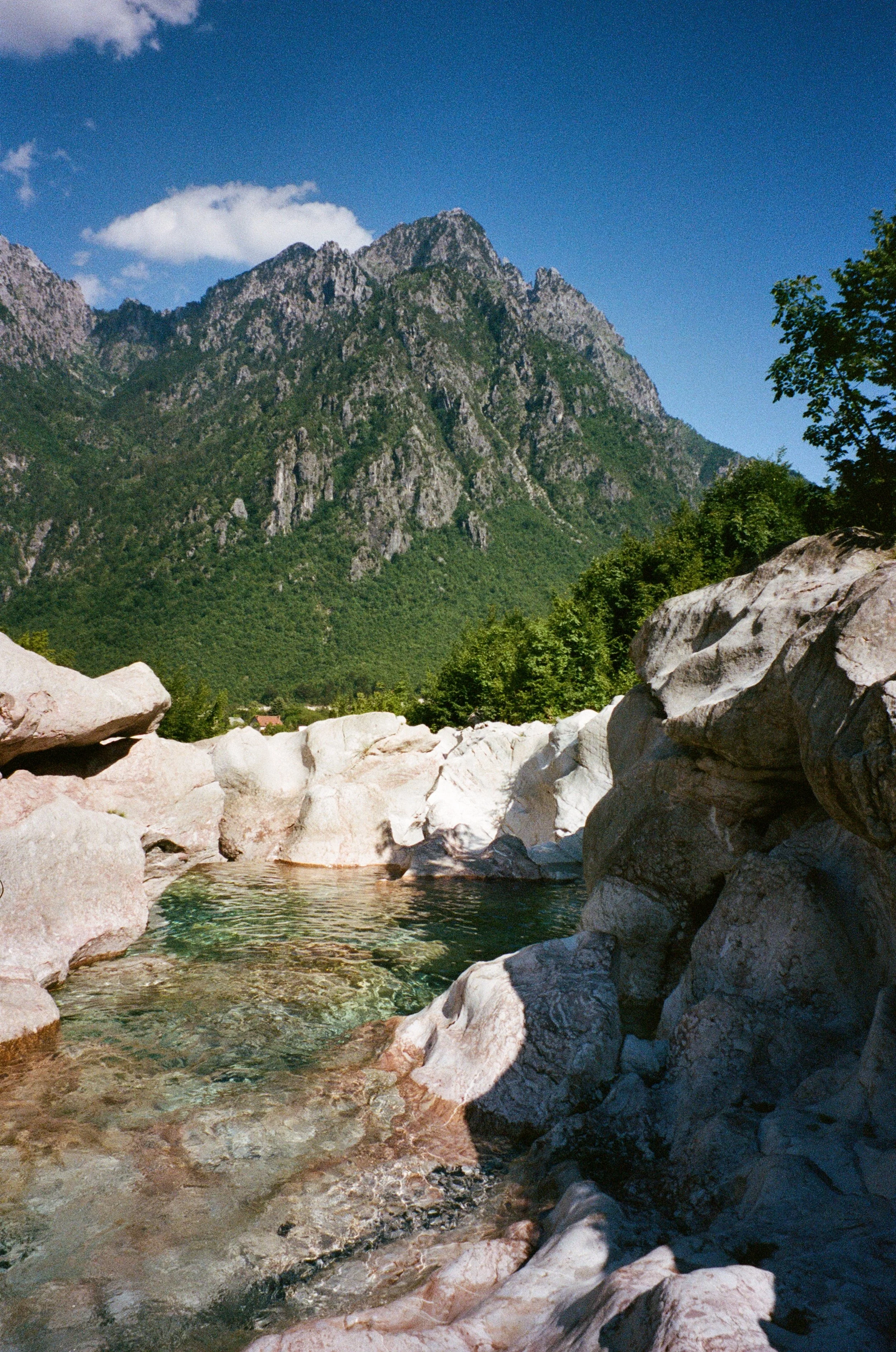 Paysage de montagne avec un ruisseau de rochers et des arbres sous un ciel bleu avec quelques nuages.