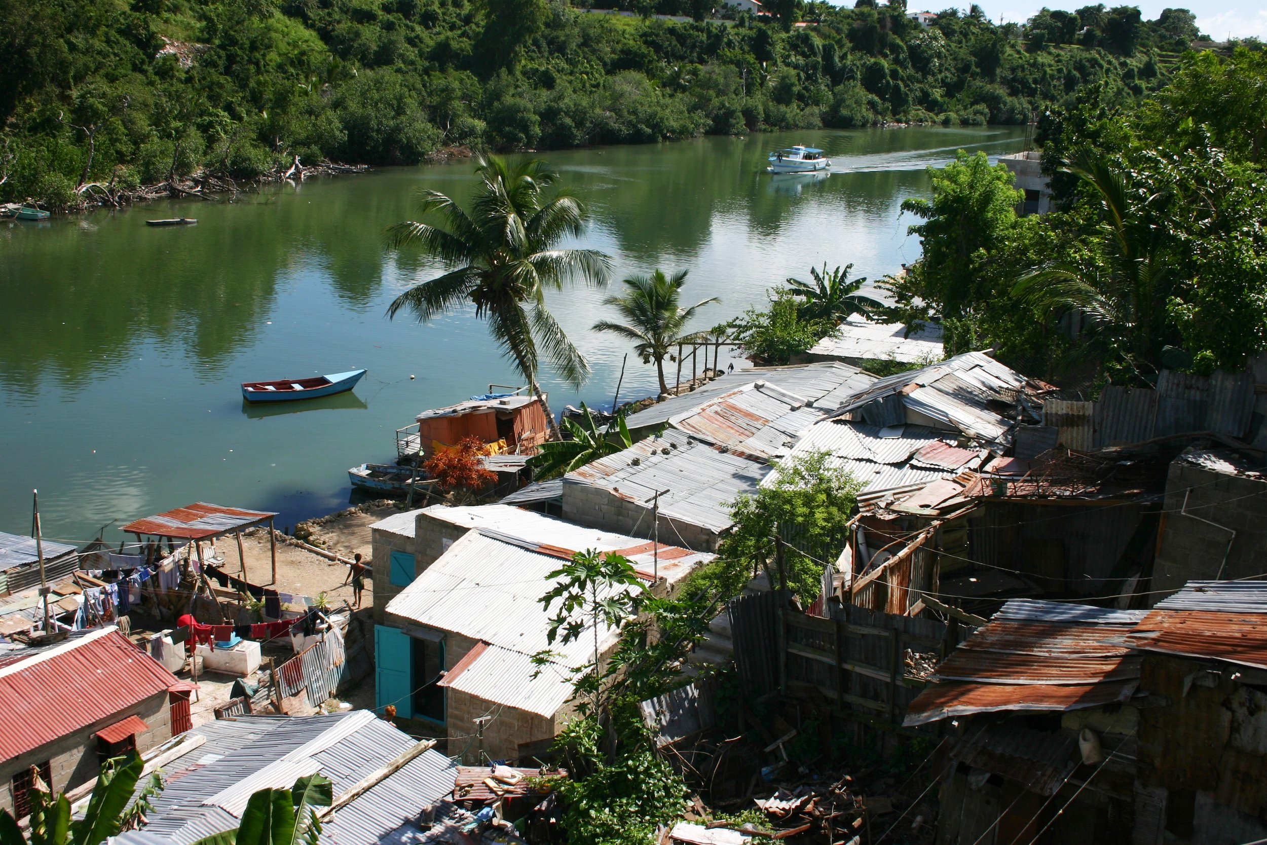 Ruelle résidentielle en bordure d'une rivière, maisons en tôles ondulées, quelques arbres dont des palmiers, Saint-Domingue, Haïti