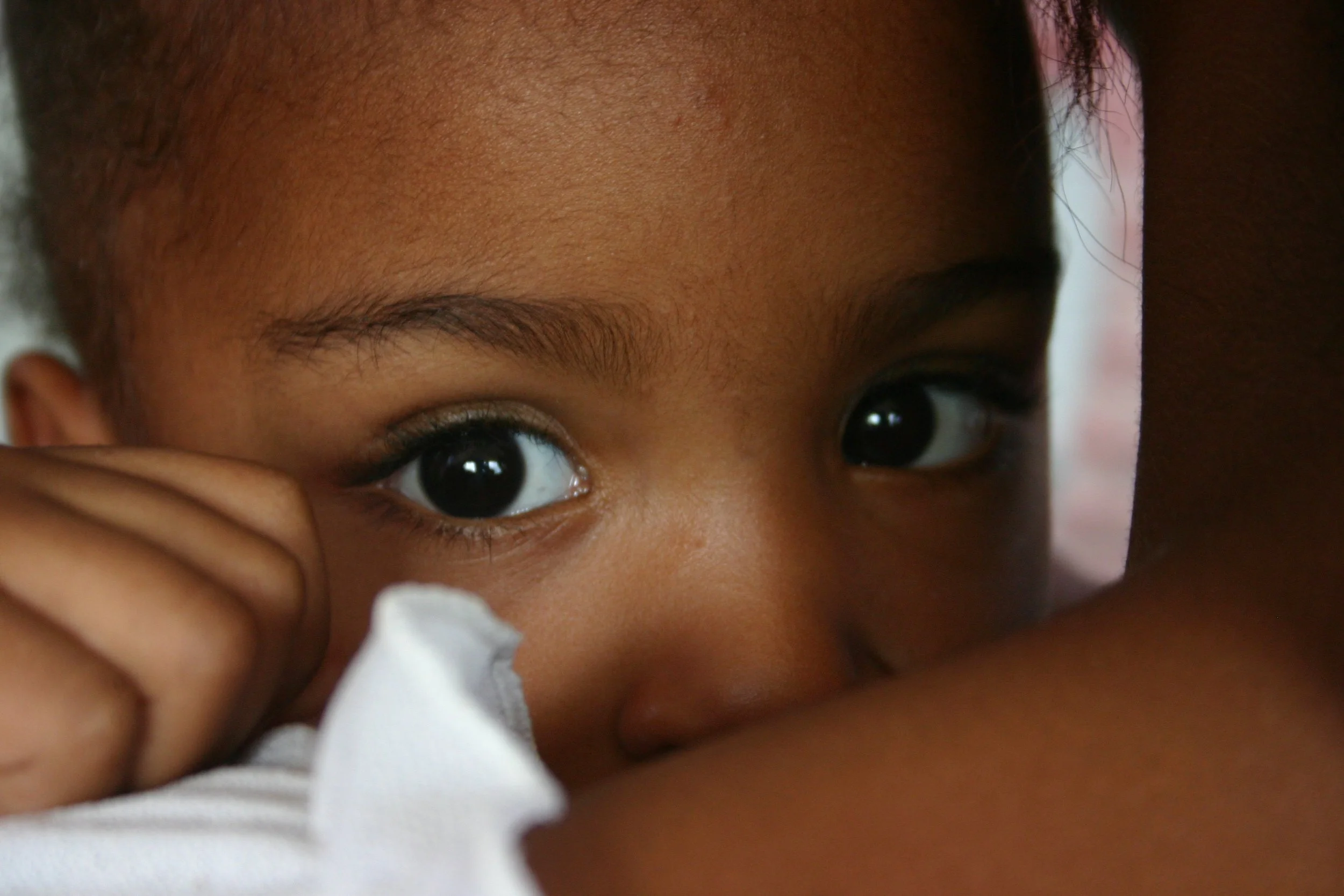 Un jeune enfant regarde fixement, portant une main près de son visage, avec un regard intense, en gros plan.
