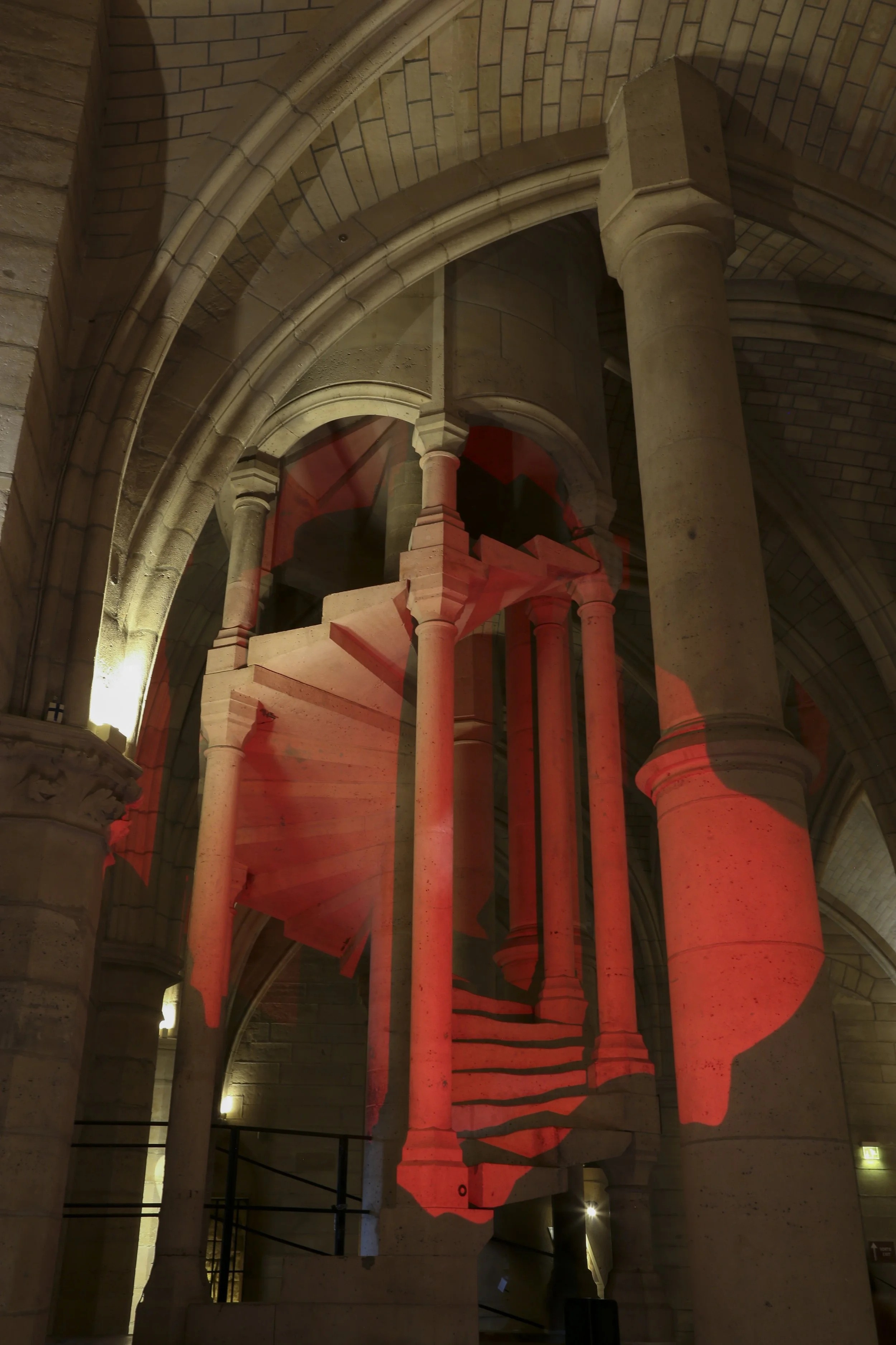 Escalier en colimaçon avec projection rouge sur la structure en pierre, dans une église ou cathédrale en pierre.
