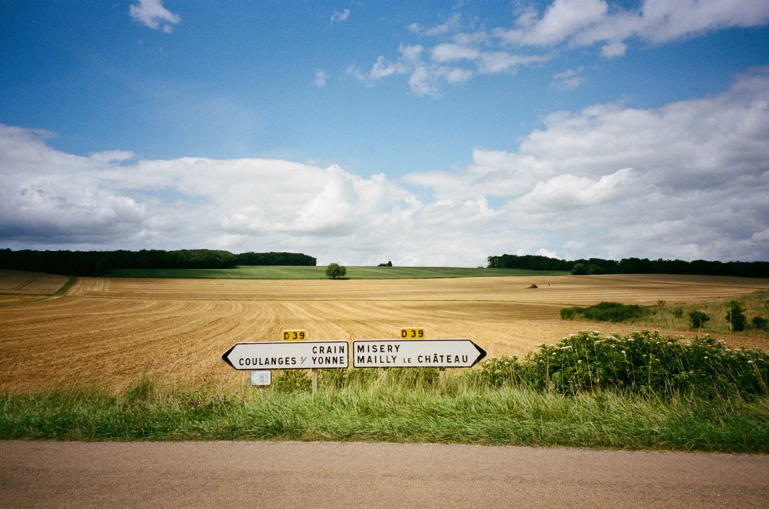 Paneau de signalisation routière en France indiquant les directions vers Crain, Coulanges sur Yonne à gauche et Misery, Mailly le Château à droite, avec un paysage de champs cultivés et un ciel partiellement nuageux en arrière-plan.