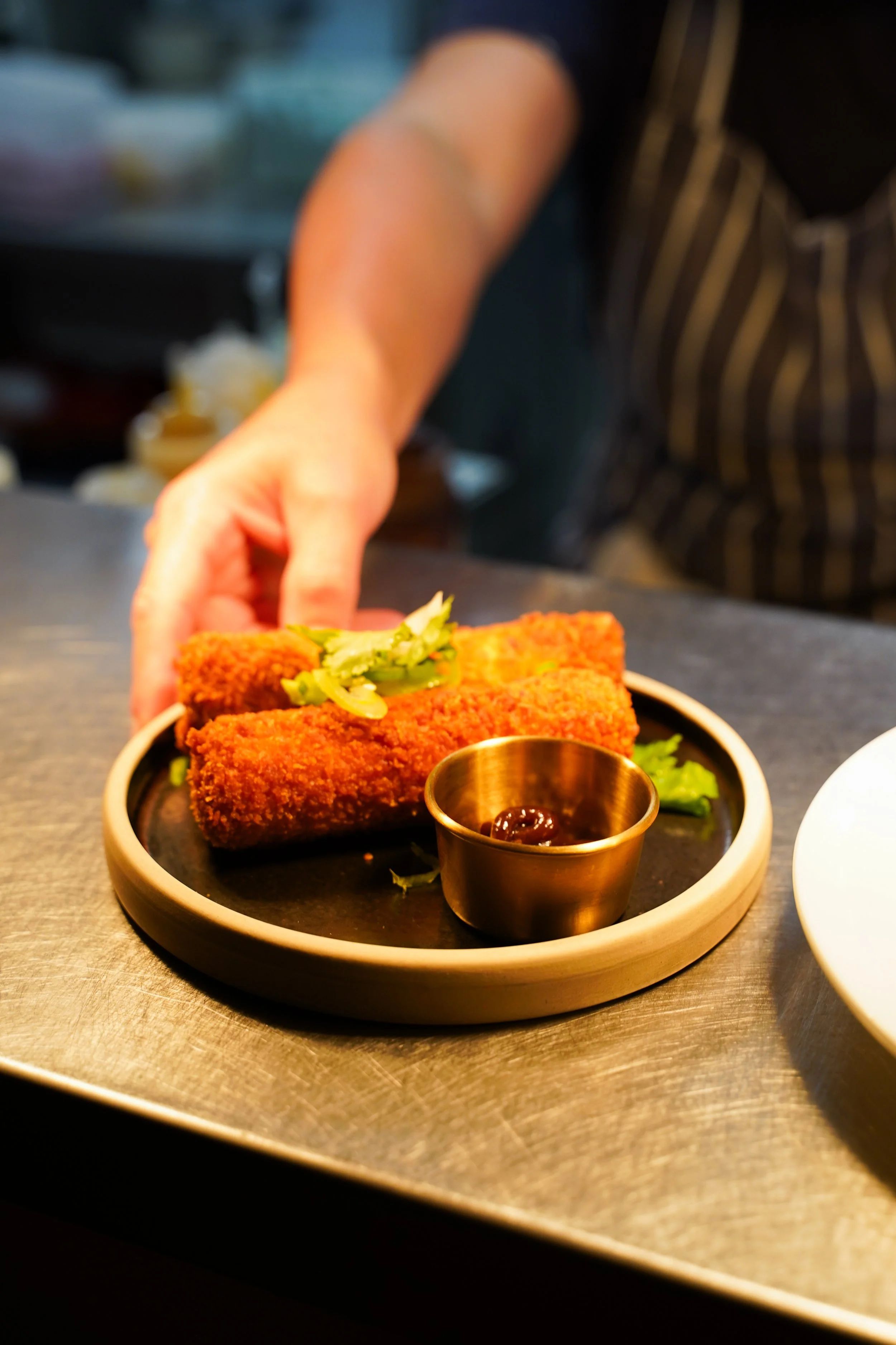 Two breaded fried fish fillets garnished with sliced green onions, served with a small cup of dipping sauce on a black plate.