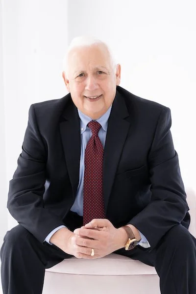Joseph Kane, Project Controls Director at Warehouses4Good, wearing a dark suit, light blue shirt, and red patterned tie, sitting and smiling at the camera.