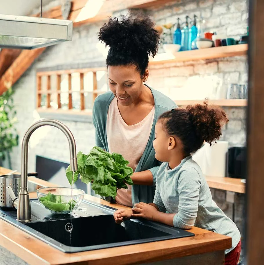A woman and a young girl washing lettuce together at a kitchen sink.