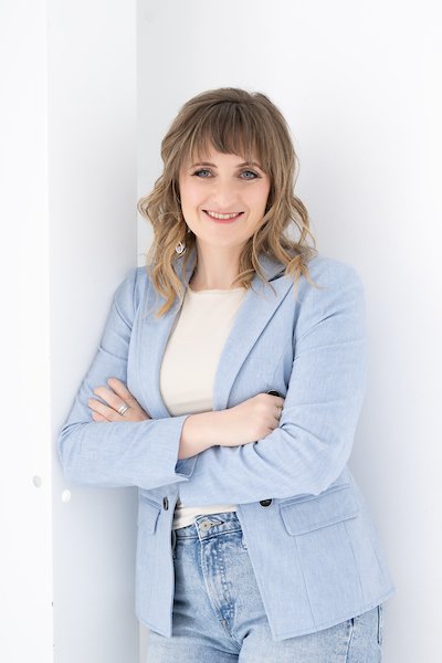 Jen Marshall, Senior Project Manager at Warehouses4Good, with shoulder-length light brown hair, dressed in a light blue blazer and white top, standing with her arms crossed and smiling against a white background.
