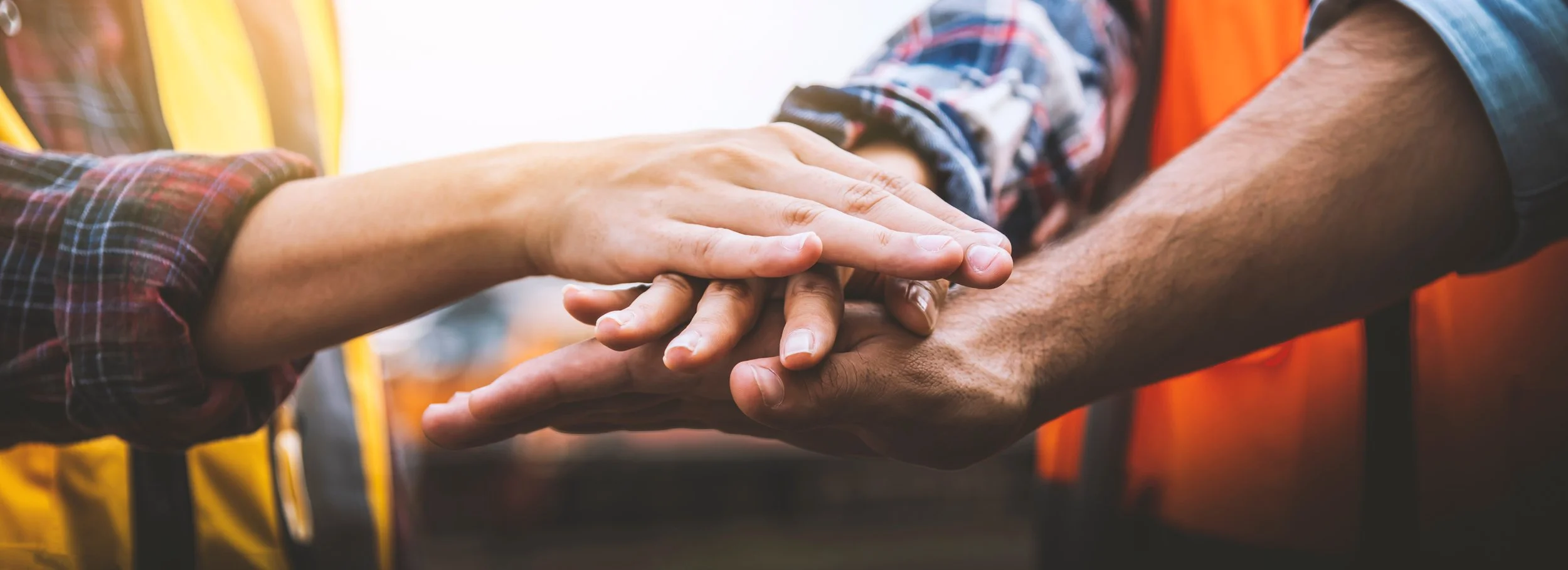 Three people are stacking their hands together at a Construction site as a gesture of unity or teamwork.