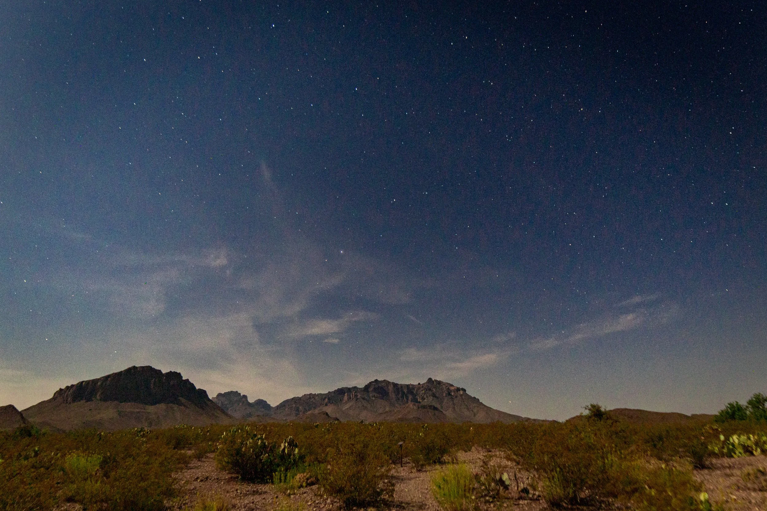 Nighttime desert landscape with distant mountains under a starry sky.
