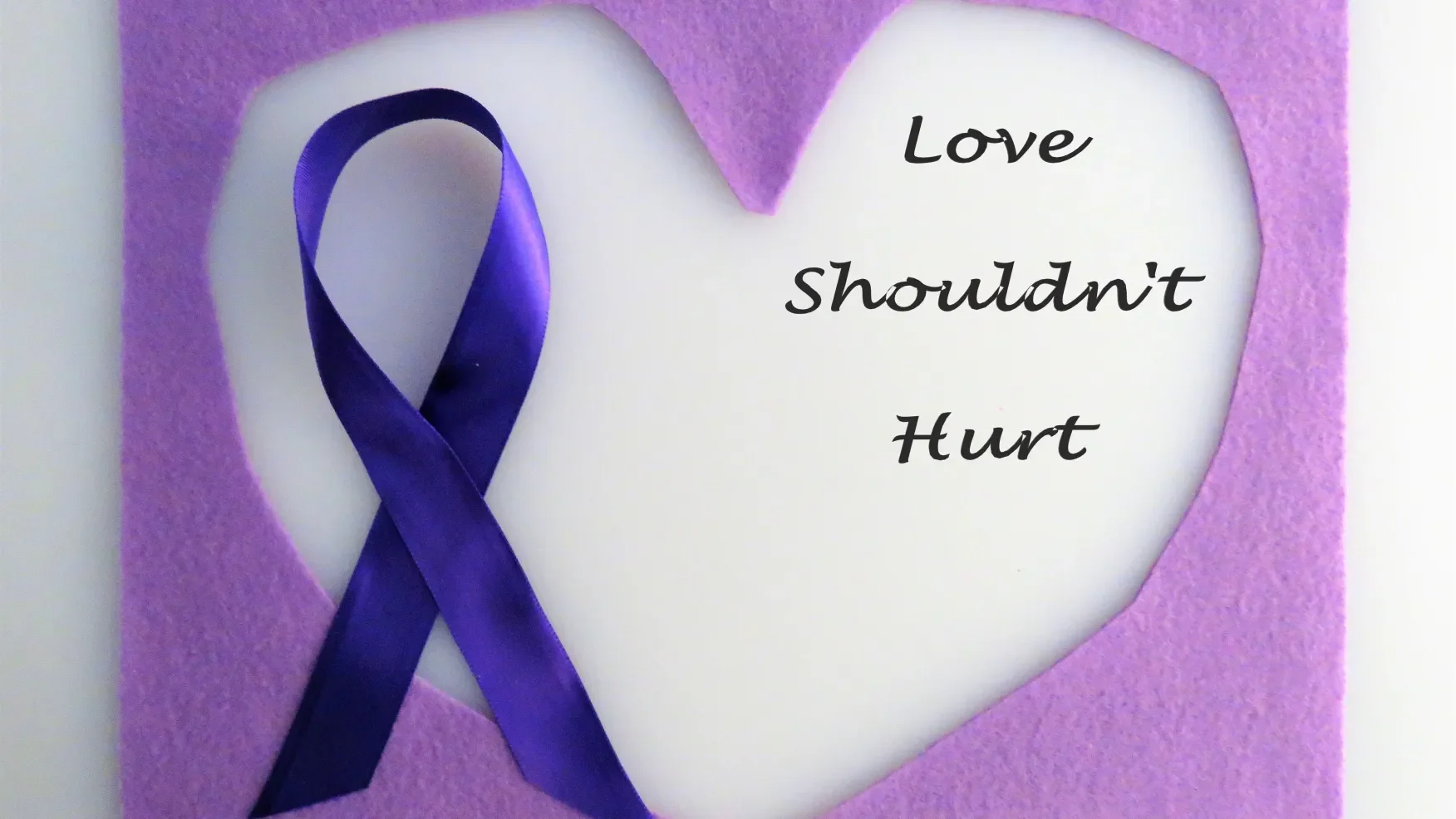 A purple ribbon attached to a white heart-shaped cutout with the words 'Love shouldn't Hurt' written on it.