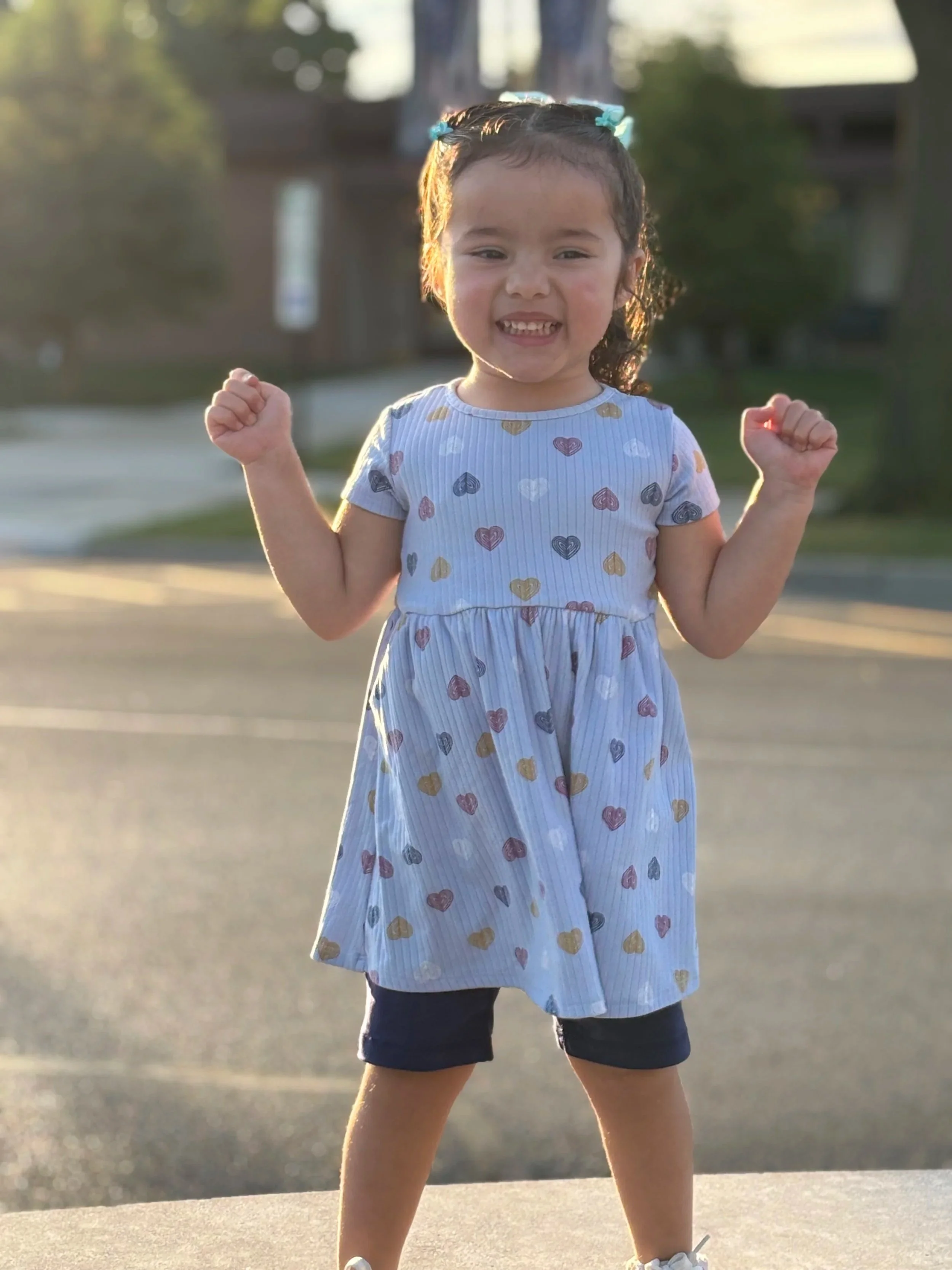 A young girl stands outdoors with her fists raised, smiling confidently.