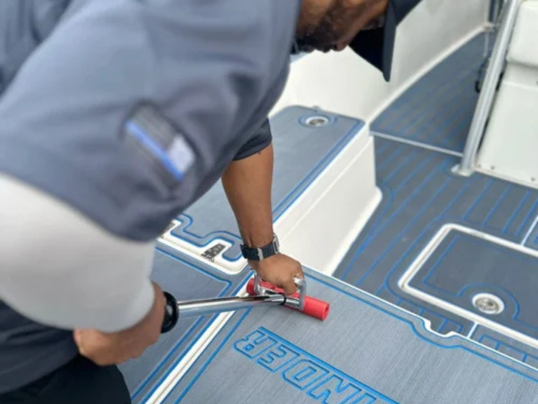 Installer using a roller to apply custom CNC-cut EVA/PE marine decking on a boat deck. The worker presses the foam flooring into place for a secure bond, demonstrating professional boat-decking installation services in South Florida.