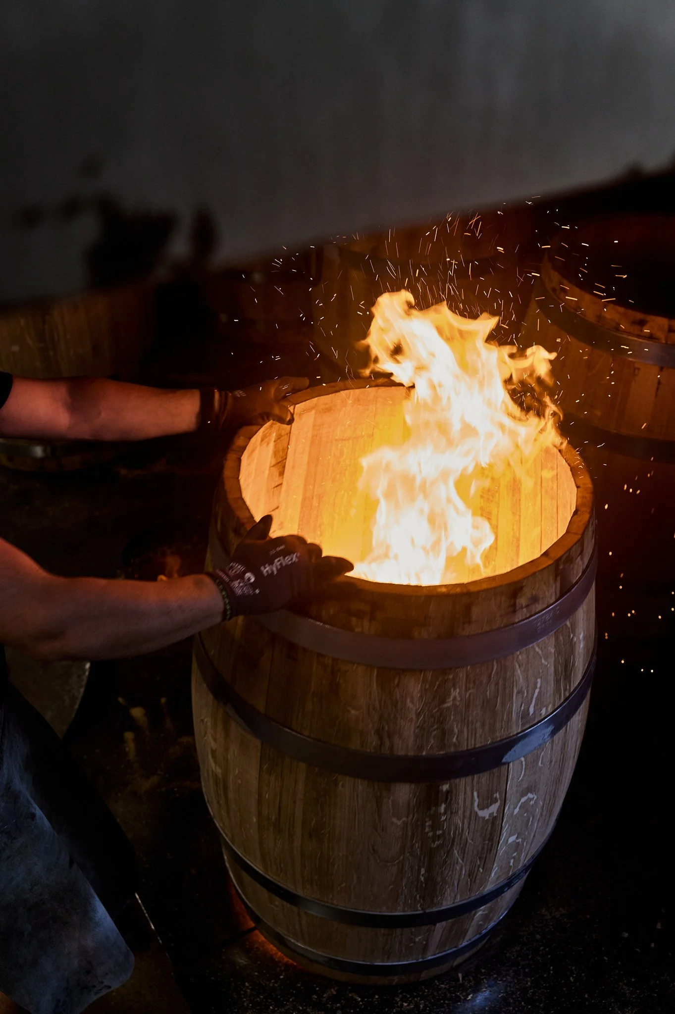Un tonneau en bois avec une flamme vive à l'intérieur, contrôlée par des mains gantées.