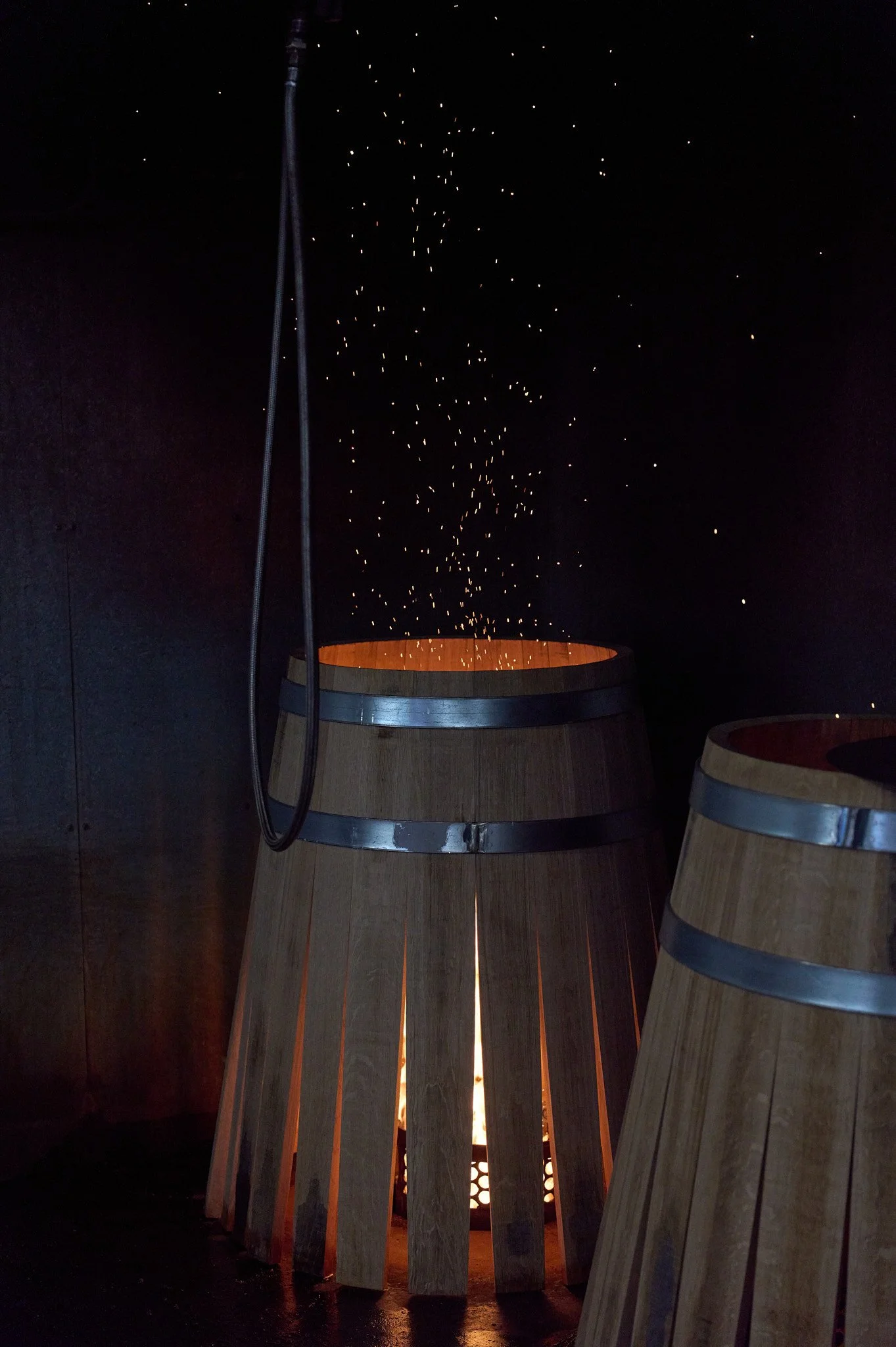 des tonneaux en bois posé sur le feu, avec des étincelles qui s'envolent dans un espace sombre.