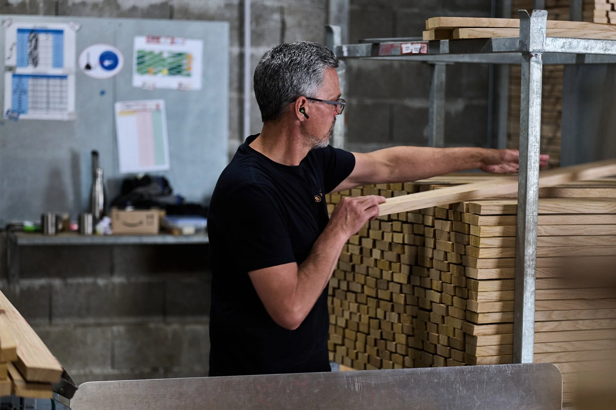 Un homme inspecte des planches de bois dans une cabane en bois, probablement dans un atelier de menuiserie.