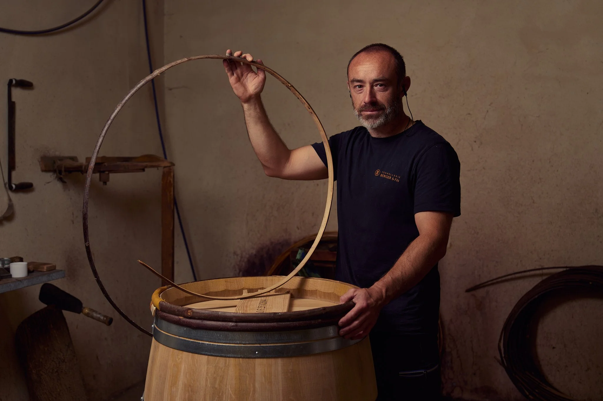 Un artisan tonnelier posant avec un cerclage bois et une barrique.