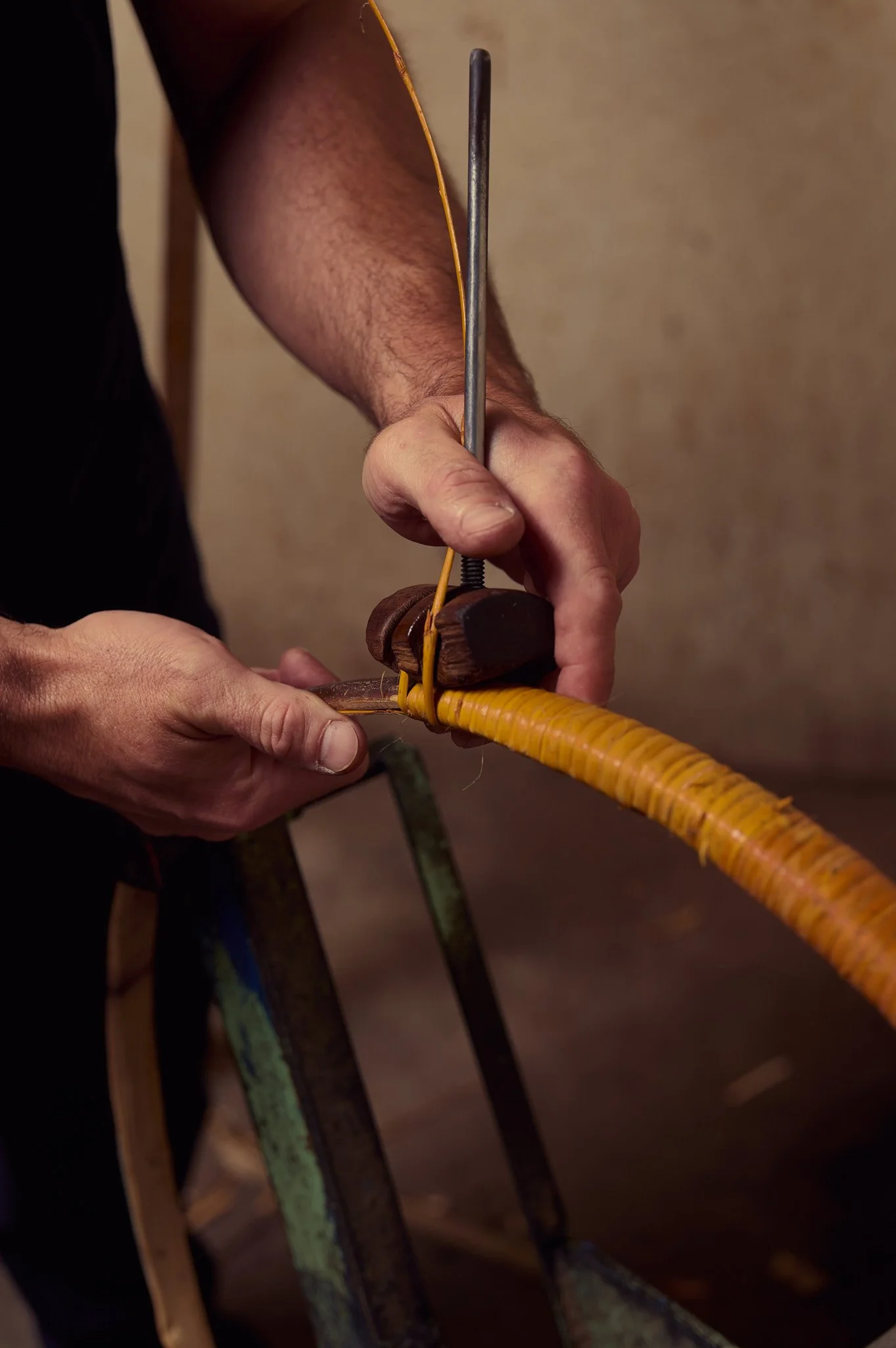 Un artisan utilise un outil pour travailler du rotin ou du bambou, enroulé autour d'une forme de bois, dans la tonnellerie.