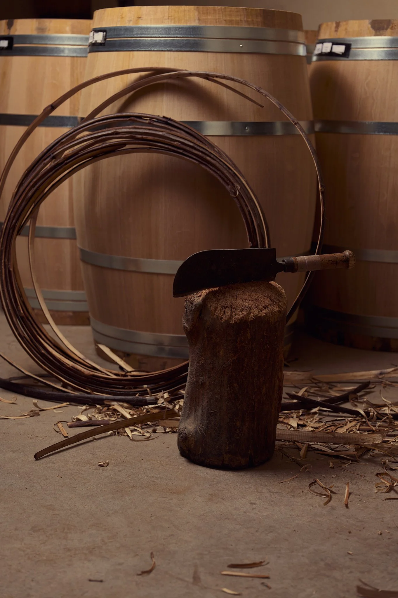 Tonneaux en bois, outil de vigneron, et copeaux en bois dans un atelier.