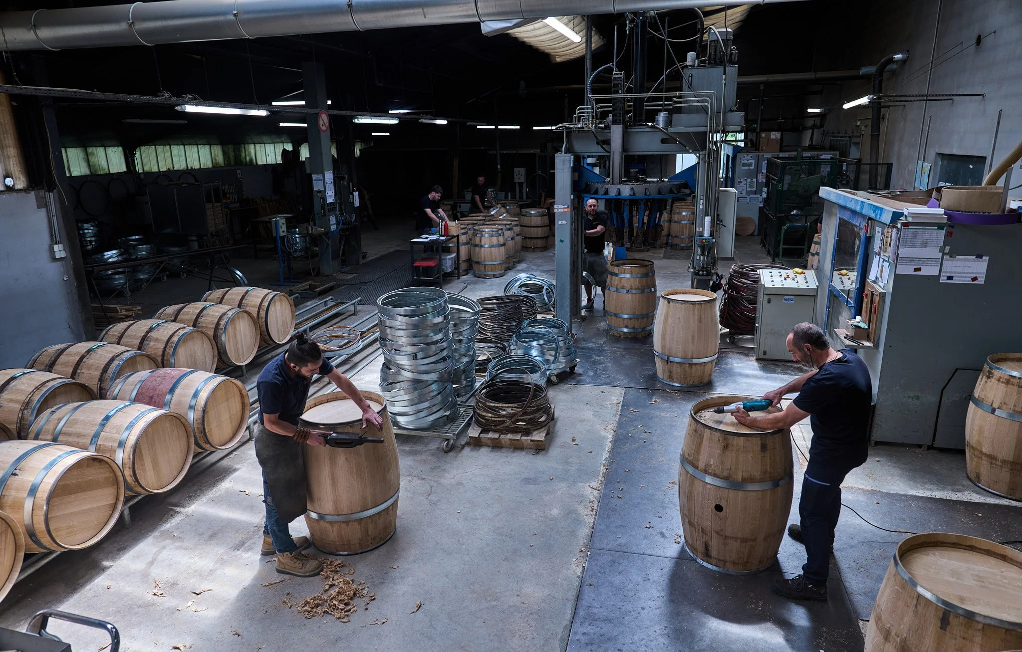 Vue d'ensemble de la l'atelier avec différents tonneliers au travail sur leurs barriques en bois.