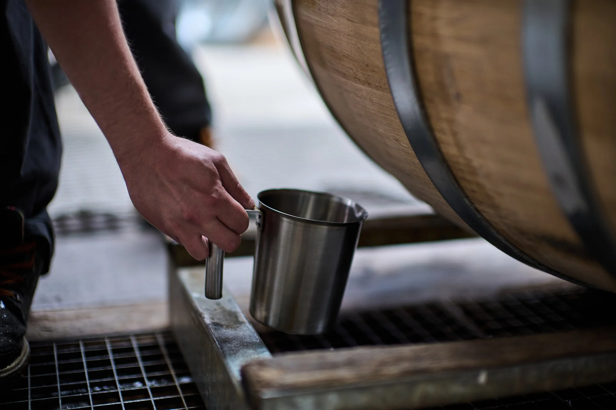 Un artisan tonnelier verse un liquide épreuve de vérification de la barrique dans un récipient en acier inoxydable.