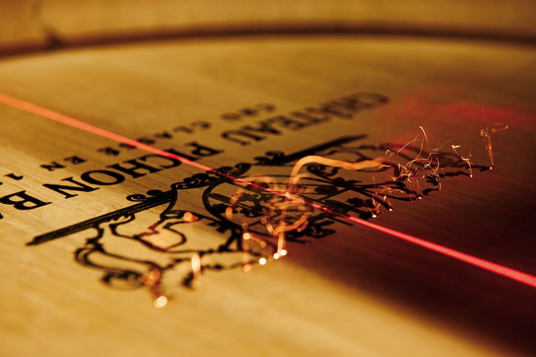 Une image rapprochée d'une plaque de bois avec une gravure et une ligne laser rouge traversant la gravure, accompagnée de étincelles de métal en fusion