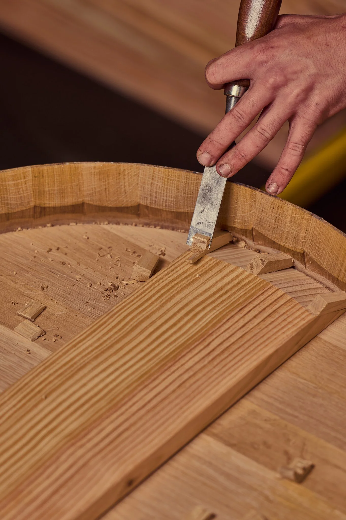 Main d'un artisan tonnelier utilisant un rabeau pour façonner un détail du fond de la barrique.