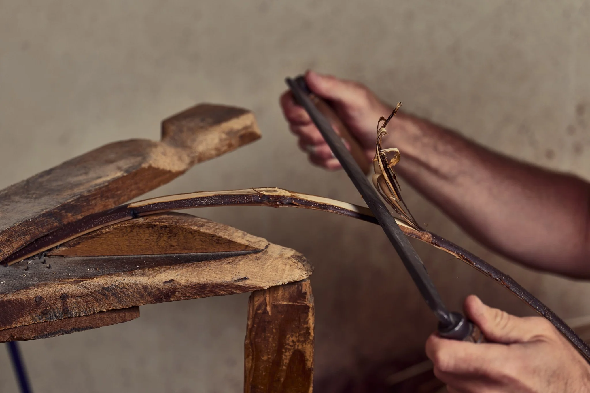 Une personne travaille avec des outils en train de plier une branche fine en bois.
