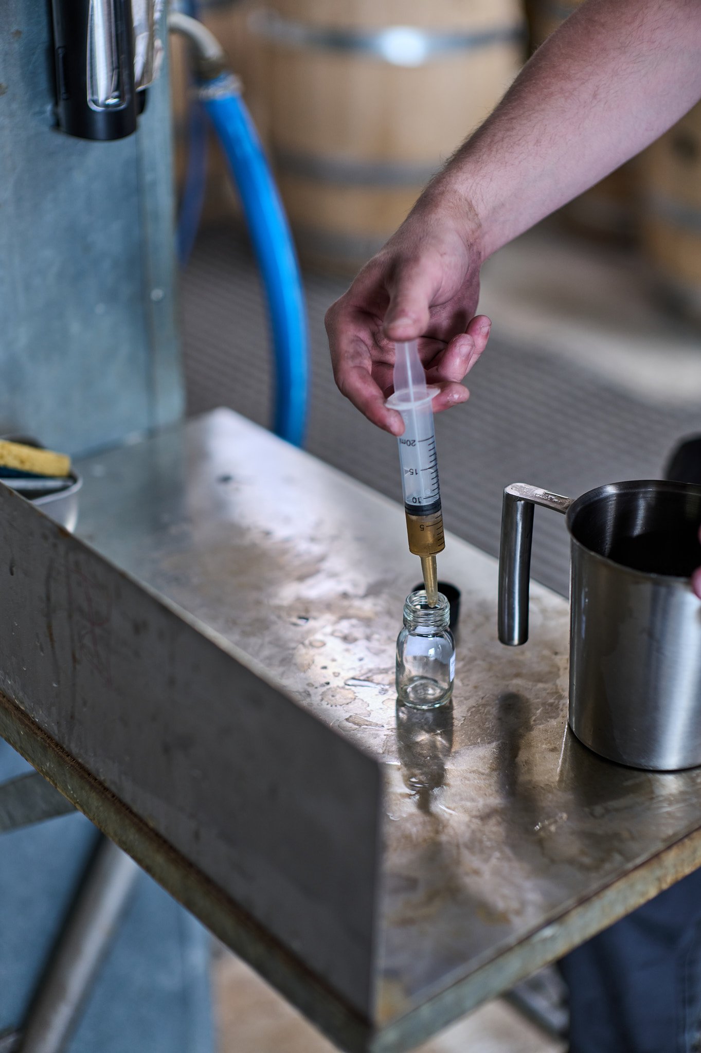 Une personne utilisant une seringue pour aspirer un liquide doré dans un petit flacon en verre sur un comptoir en métal.