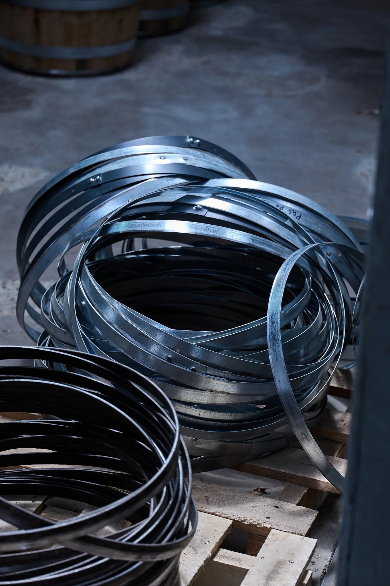 Cercles métalliques empilés sur un sol en béton, certains posés sur des palettes en bois.