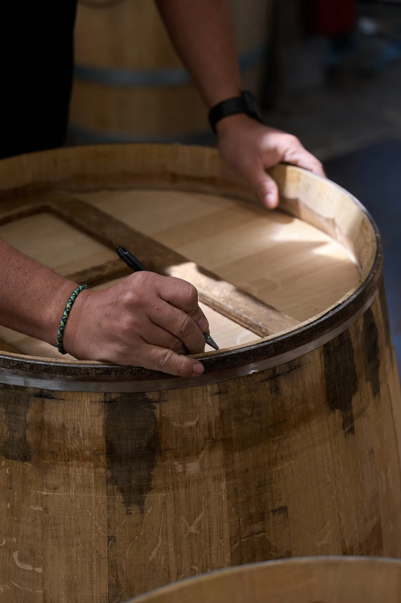 Une personne en train de dessiner ou de marquer à la main l'intérieur d'un grand fût en bois, probablement en train de fabriquer ou de réparer un tonneau.