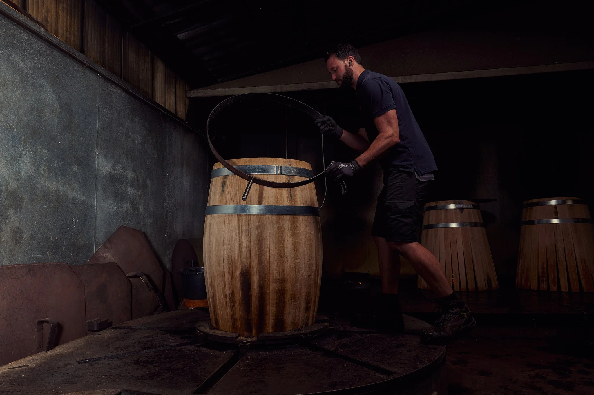 Un artisan tonnelier au travail avec une barrique en bois en cours de fabrication.