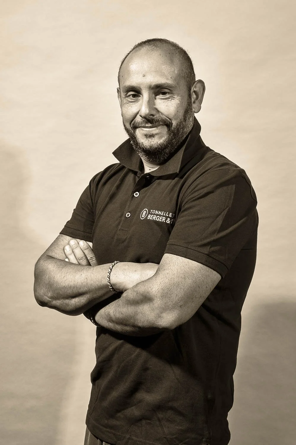 Homme souriant, aux bras croisés, portant un polo noir avec le logo de Tonnellerie Berger & Fils, sur un fond neutre.