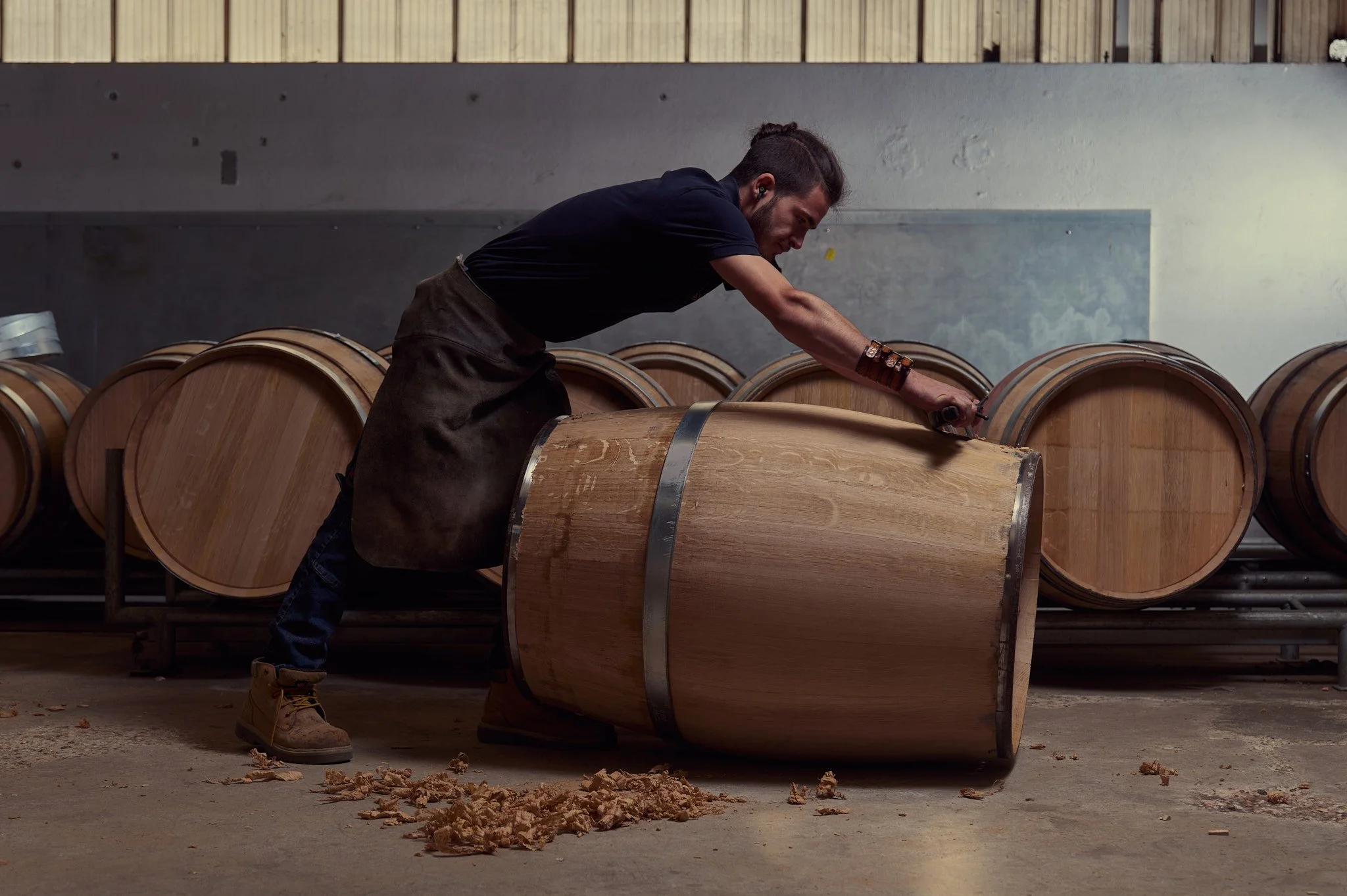 Un artisan tonnelier en train de guistrer une barrique dans l'atelier.