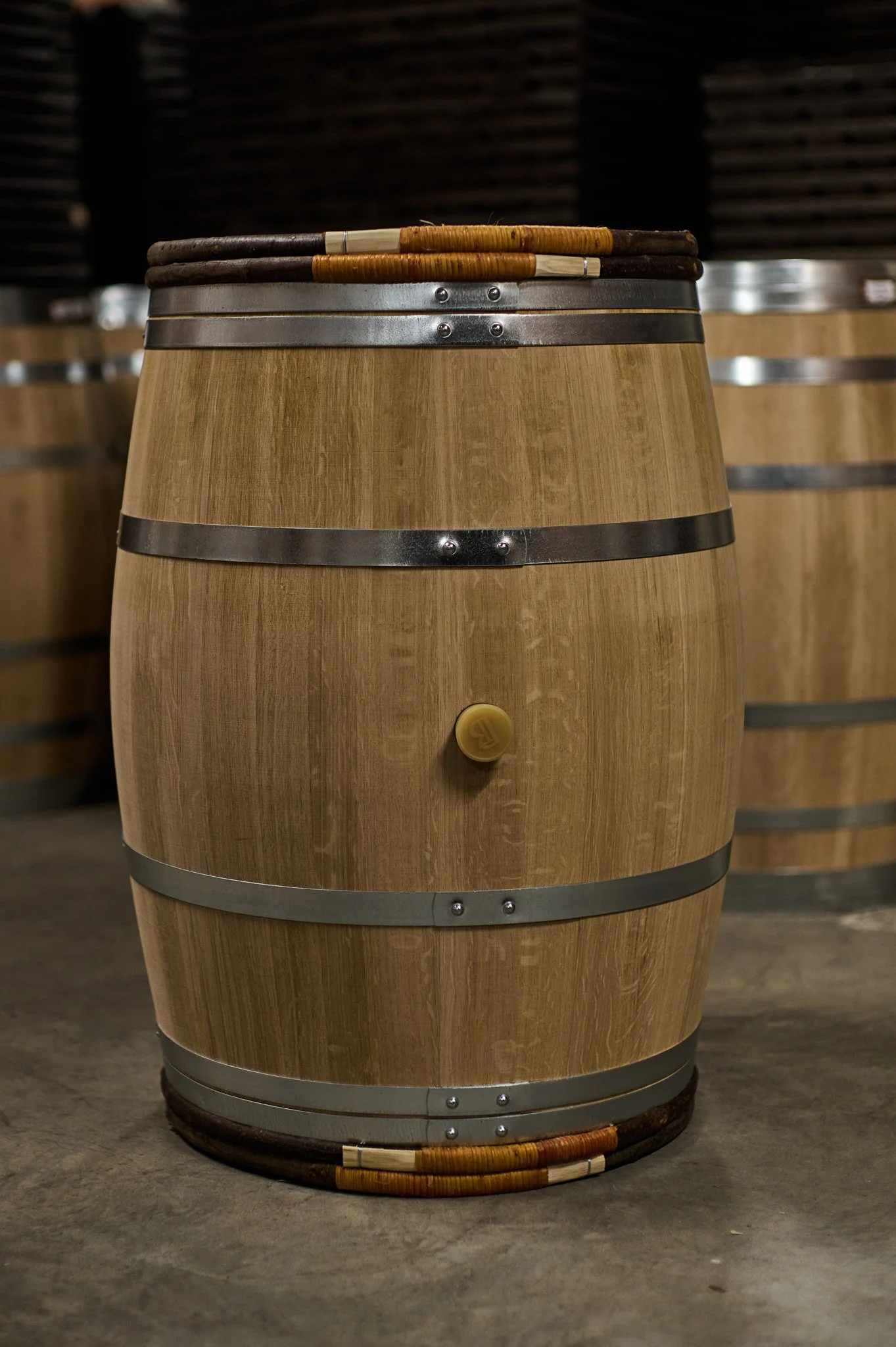 Une barrique en bois utilisée pour le vieillissement du vin, avec un robinet. Autres barriques visibles en arrière-plan.