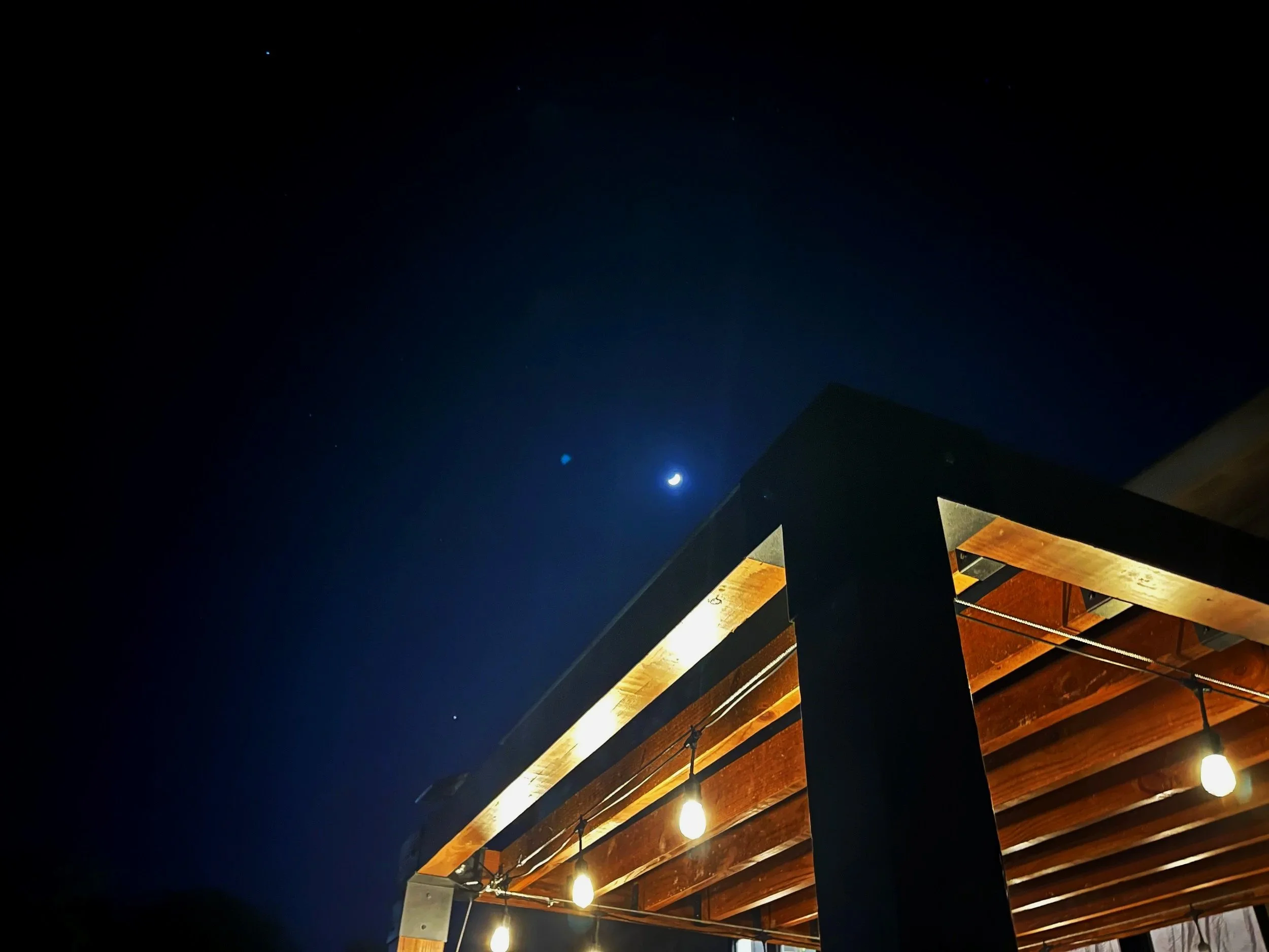 modern pergola under starry night sky with solar powered string lights and black, steel corner brackets installed by Lyoness Industries