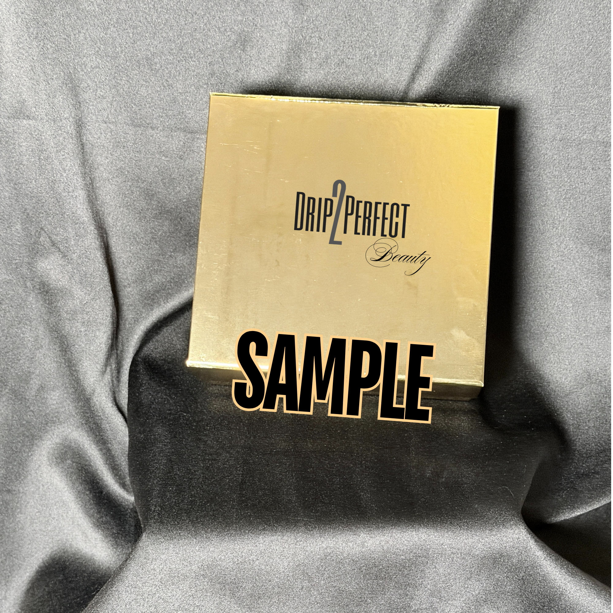 Gold box with the words "Drip2Perfect Beauty" and the word "Sample" on a black fabric background.