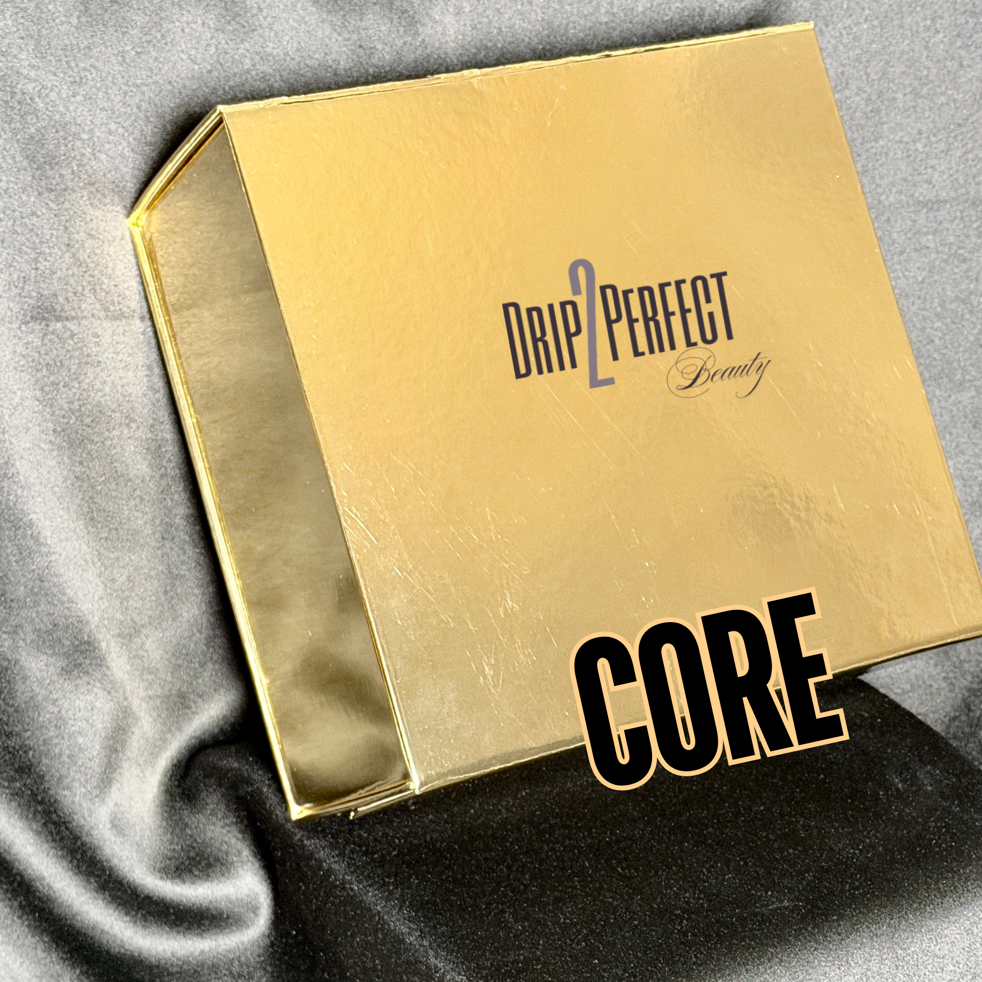 Gold box labeled 'Drip2Perffect Beauty' resting on black satin fabric, with the word 'GORE' overlaid in bold black letters.
