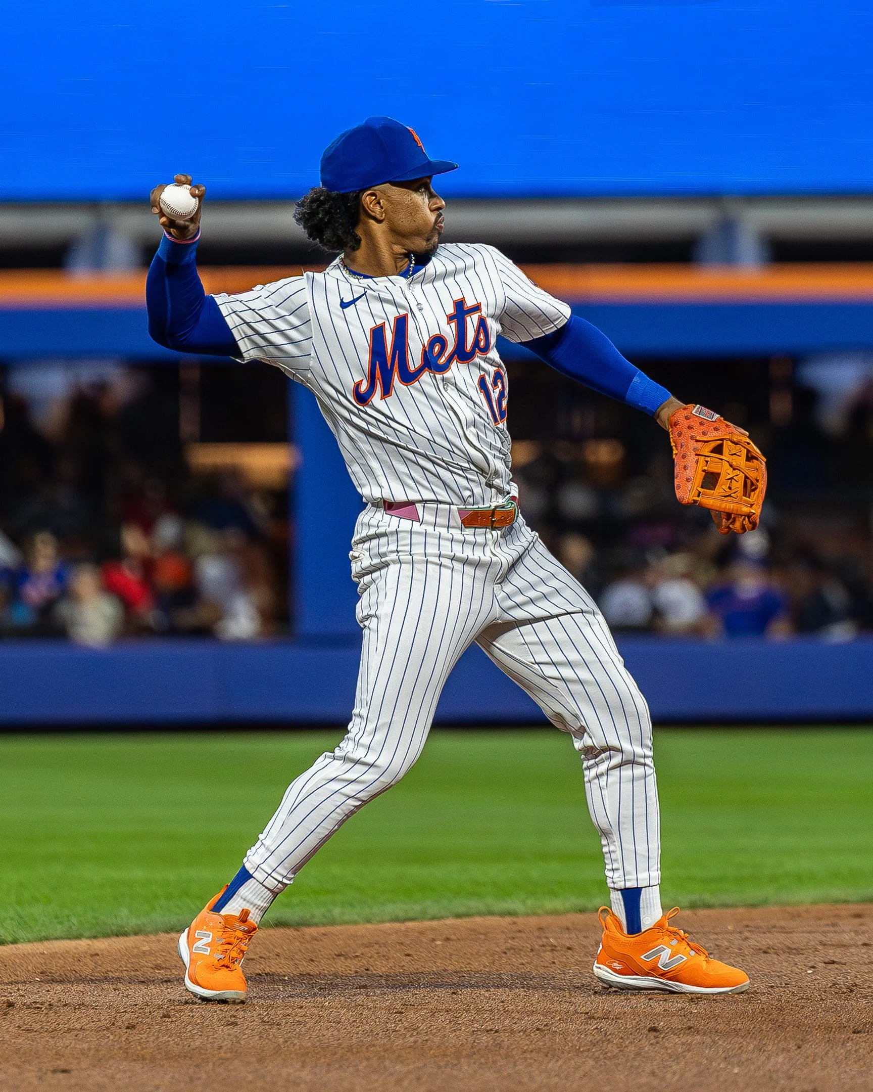 A baseball player from the New York Mets, wearing a striped uniform, a blue cap, and orange cleats, preparing to throw a pitch on the mound during a game.