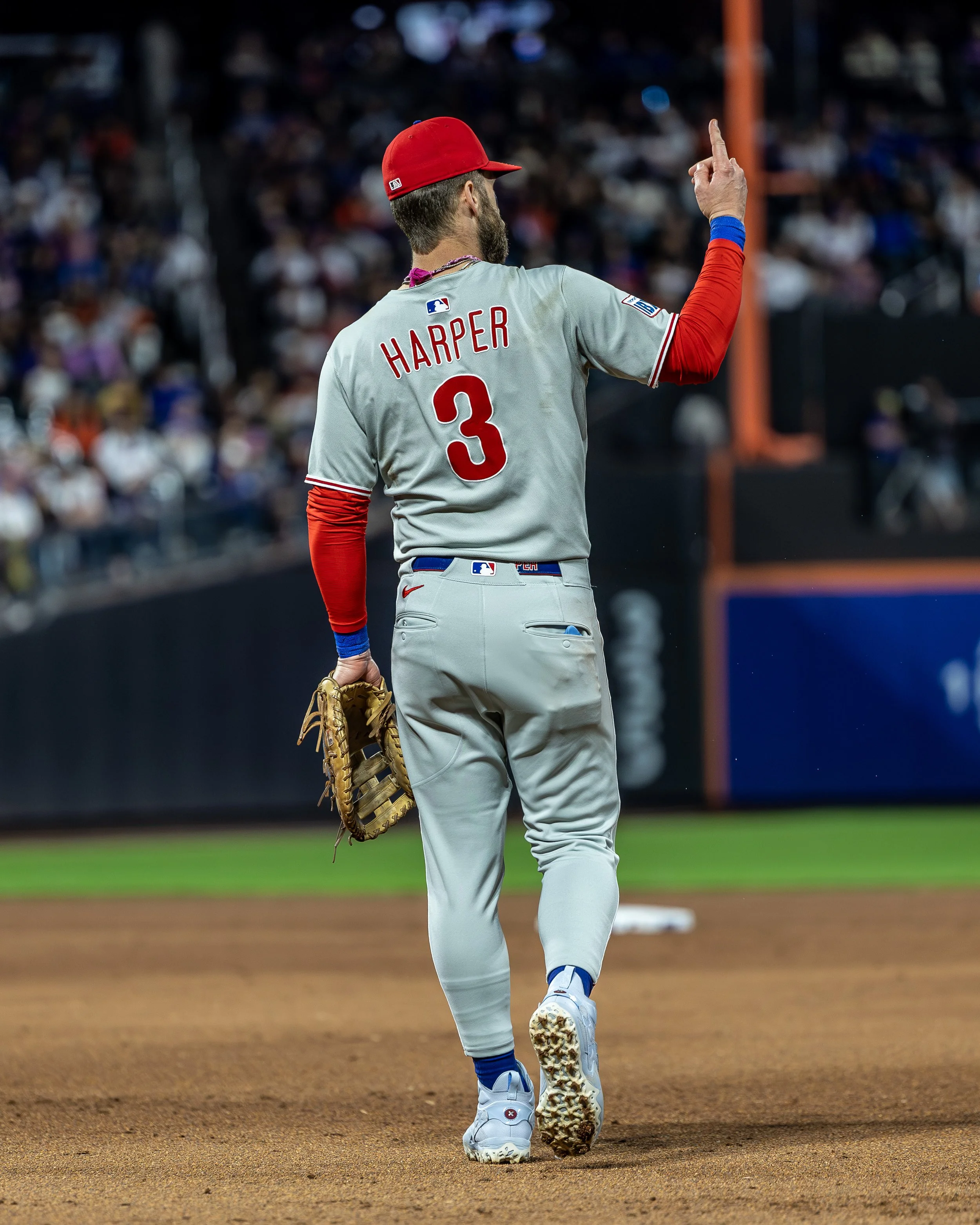 A baseball player with the last name Harper wearing a gray uniform and a red cap, holding a baseball glove, on a baseball field with a crowd in the stands.