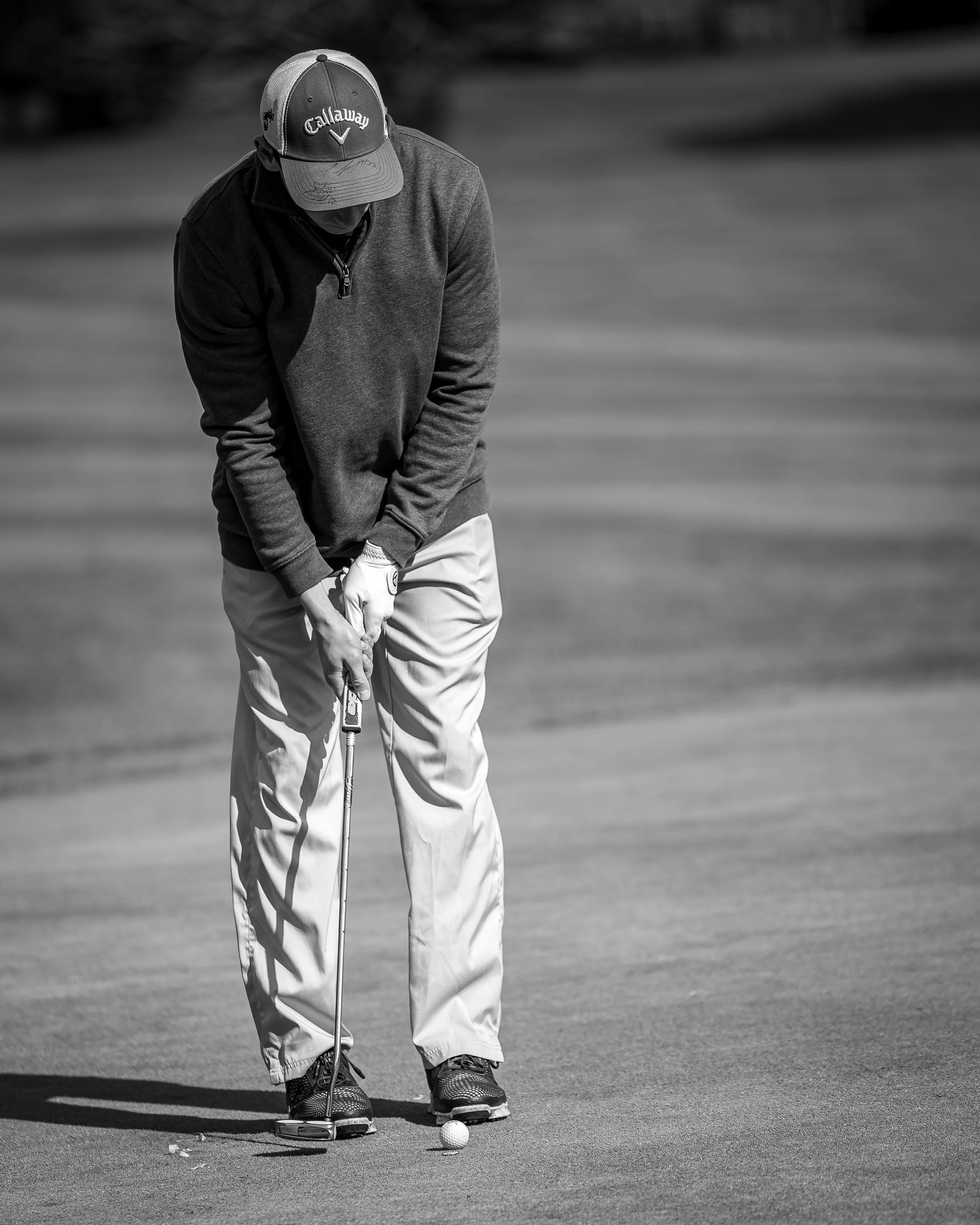 A man in a cap, jacket, and slacks playing golf, preparing to putt on the green.