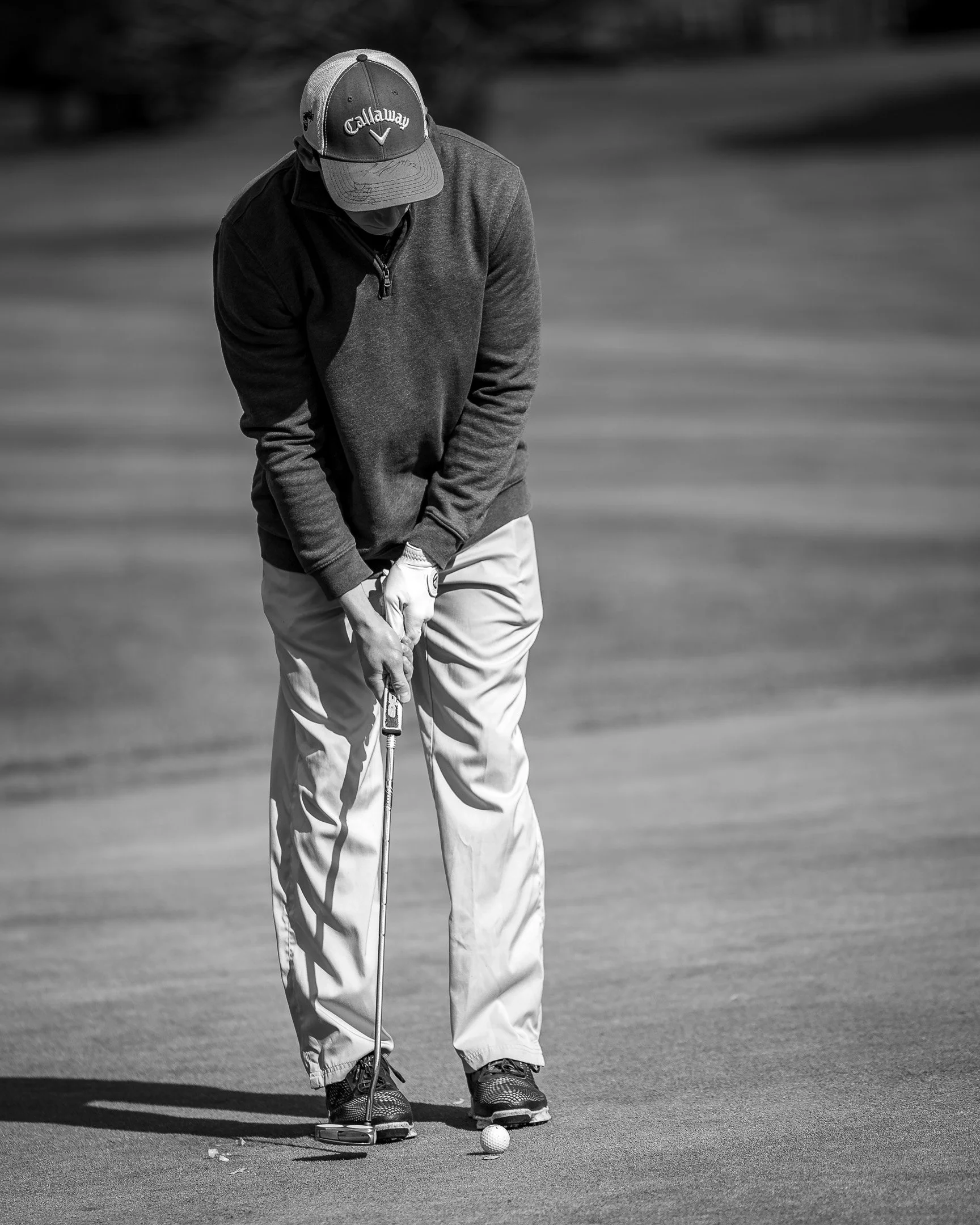 A man playing golf on a golf course, preparing to putt, dressed in casual golf attire.