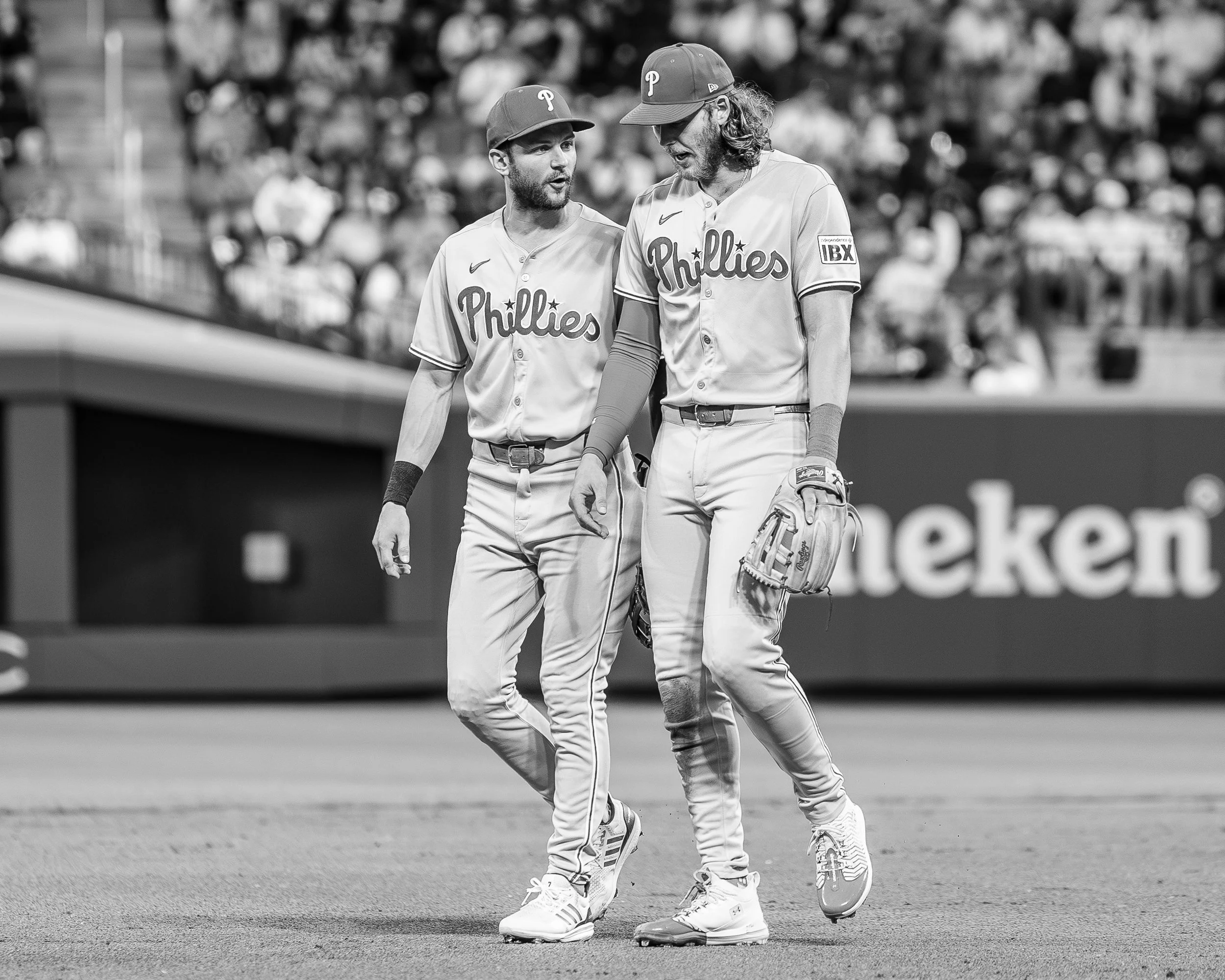 Two baseball players in Phillies uniforms walking and talking on the field during a game, with a crowd in the background.