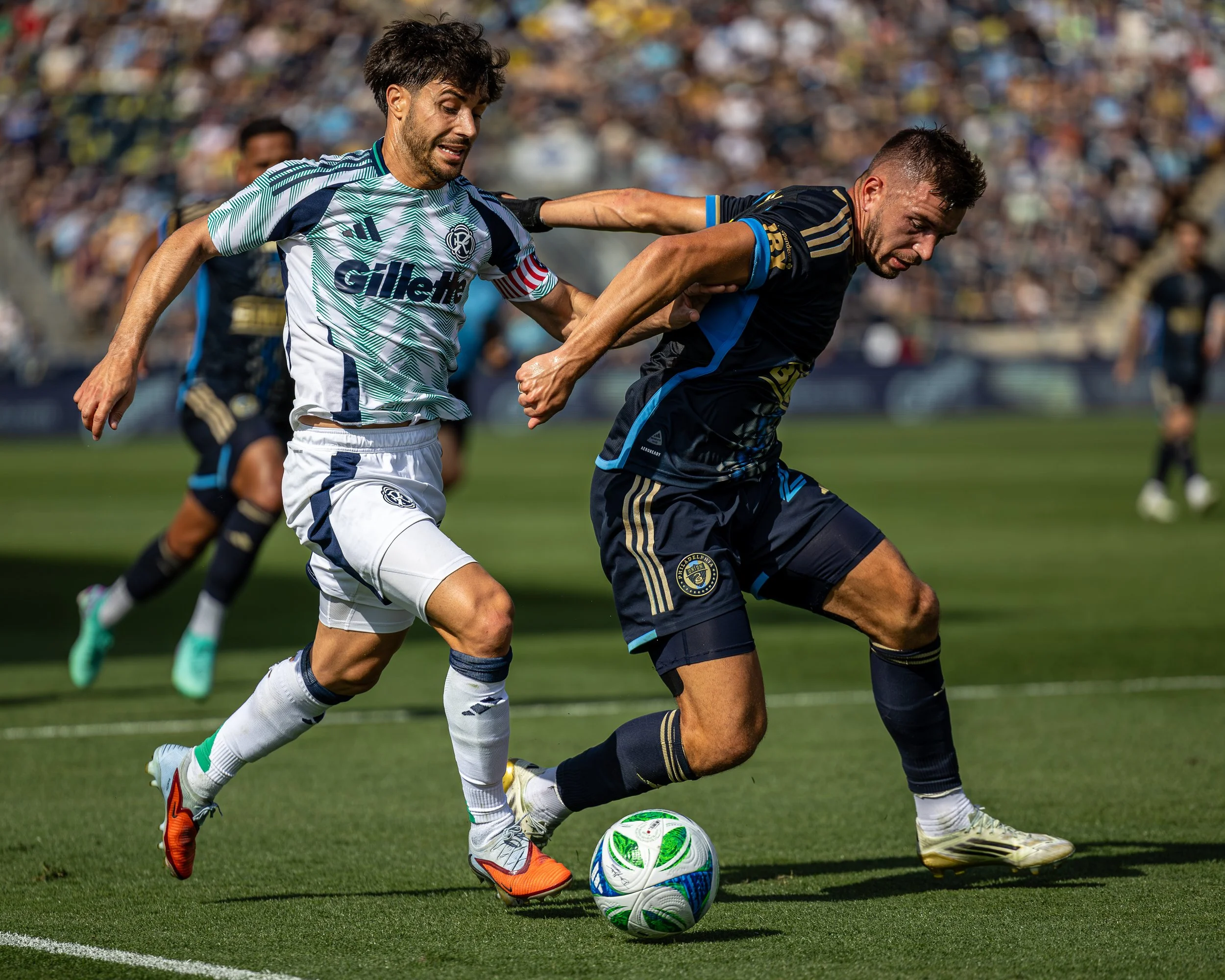Two soccer players competing for the ball on the field during a match, with a large crowd in the background.