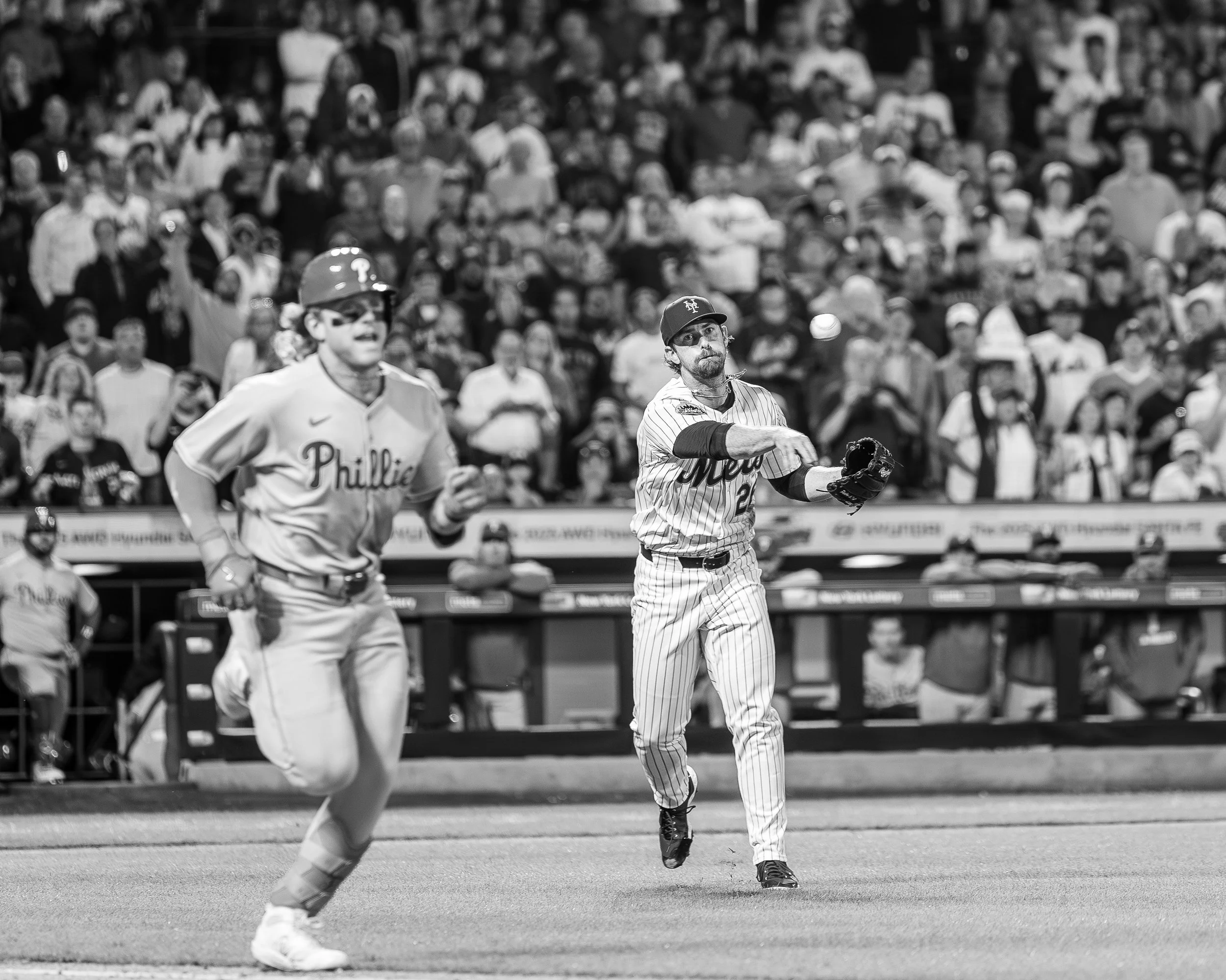 Two baseball players from different teams running on the field during a game, with a large crowd watching from the stands in the background.