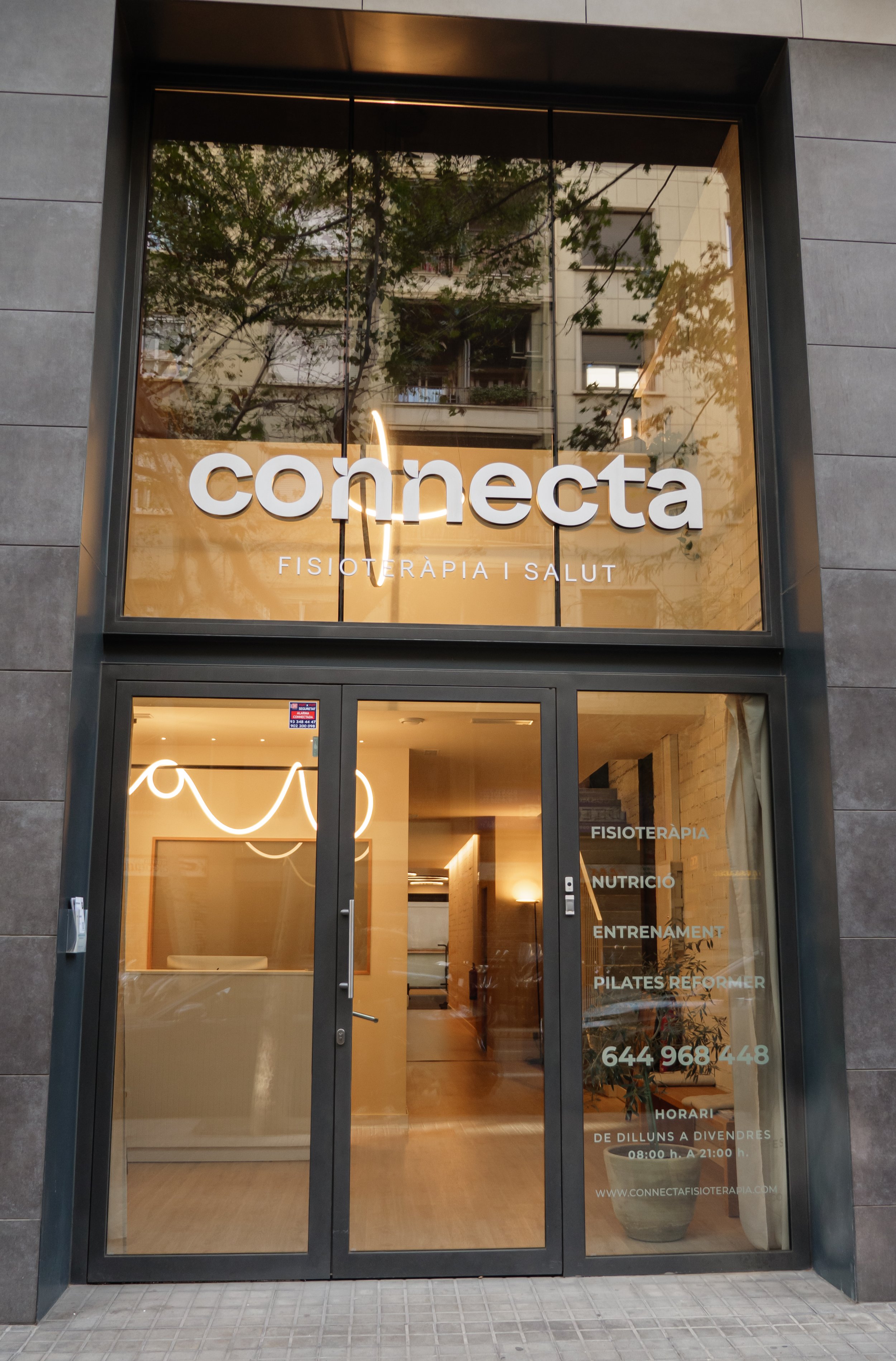 Fachada de un centro de fisioterapia y salud llamado 'conecta', con letras grandes en la parte superior y detalles en letras blancas en la puerta que indican servicios como fisioterapia, nutrición, entrenamiento y Pilates reformer, además de un número de contacto y horario de atención.