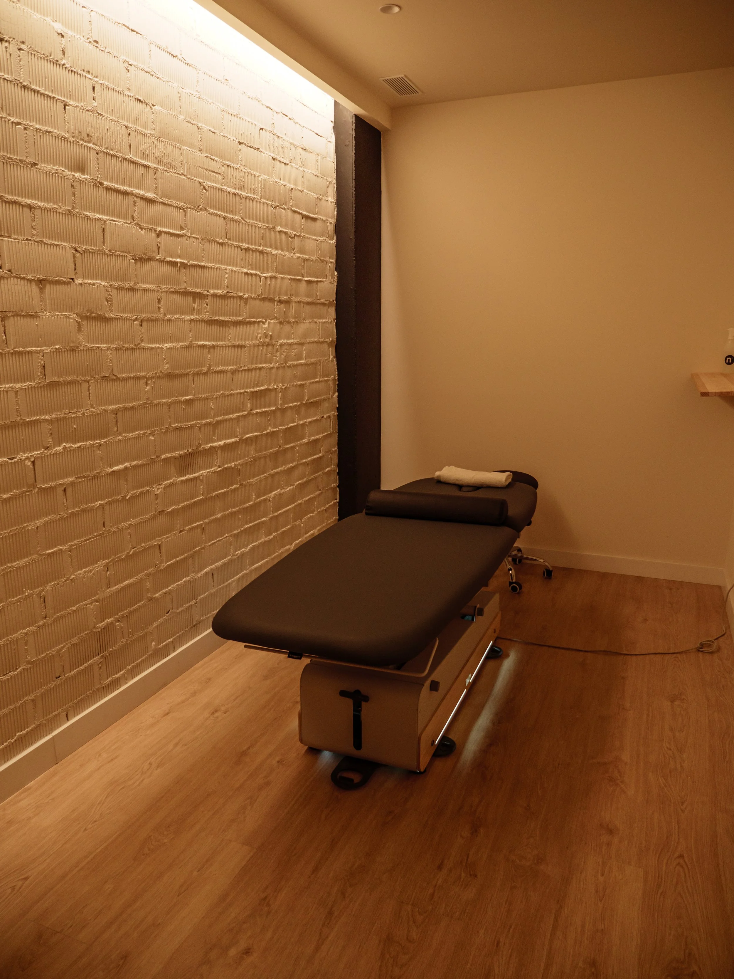 Una camilla de tratamiento en una sala con paredes blancas y piso de madera, en un ambiente tranquilo y ordenado.