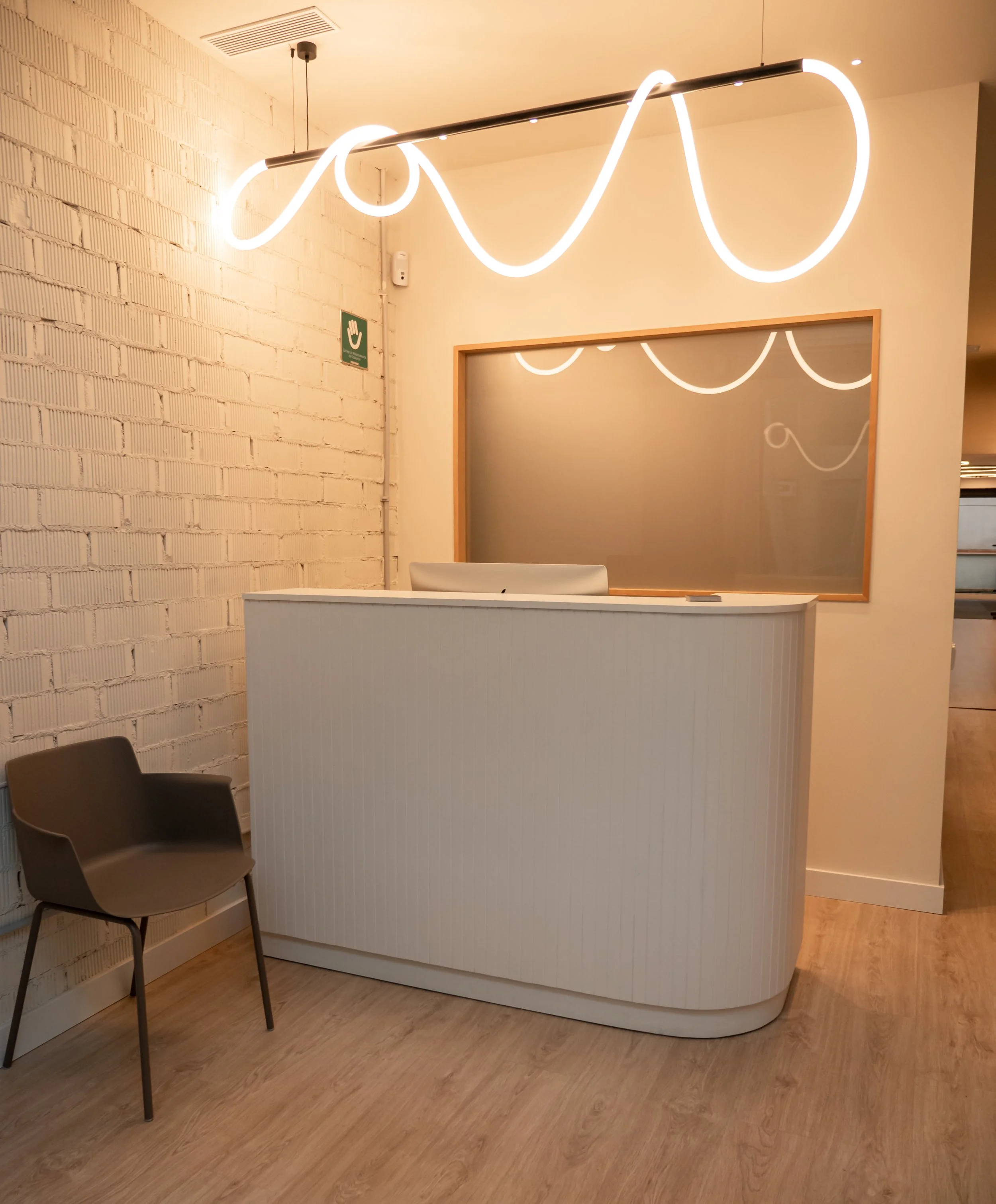 Mostrador de recepción en un espacio moderno con lámpara de neón en el techo y silla de color gris.