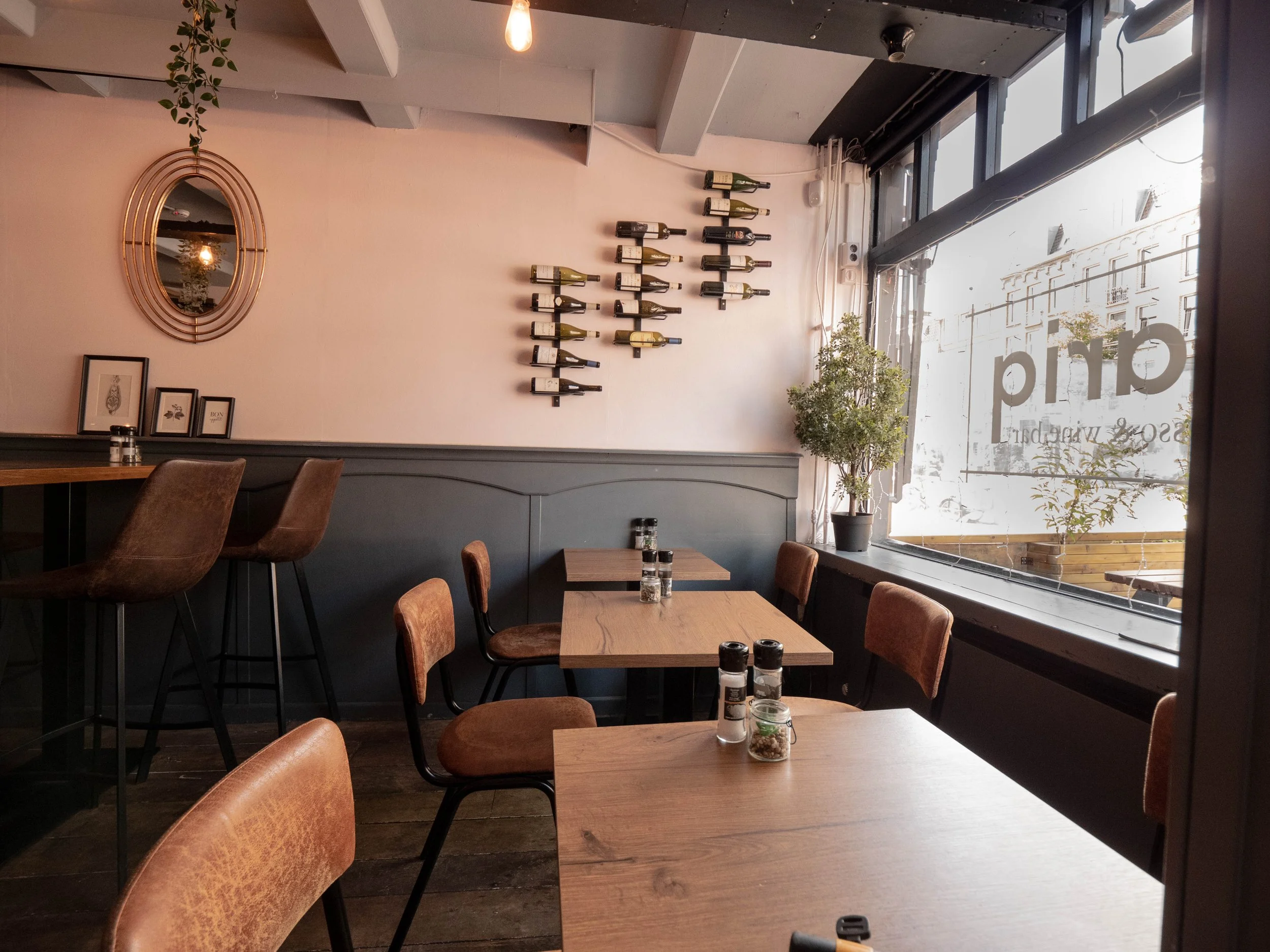 Interior de un café con mesas de madera, sillas de estilo vintage y plantas en las ventanas.