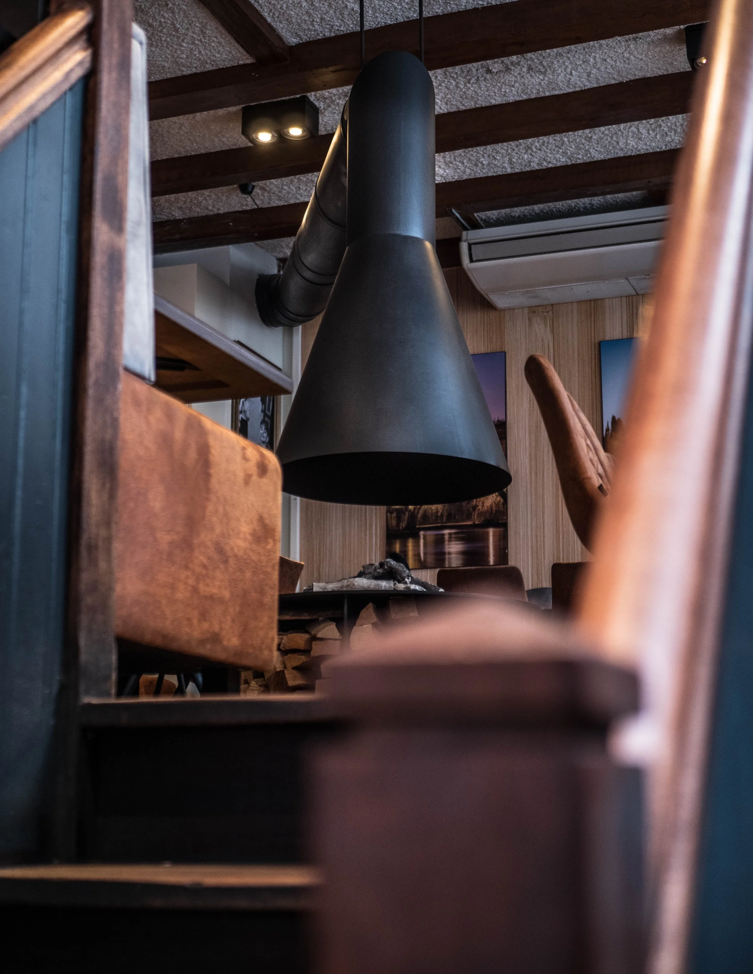 Vista de interior de restaurante con estructura de madera, chimenea negra con tubo de escape, y paredes de madera decoradas con cuadros.