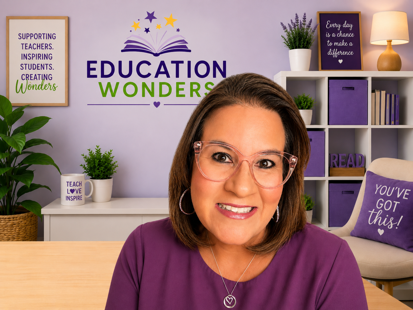 Woman with brown hair and glasses smiling in a colorful classroom or office setting with educational and motivational signs and decor.