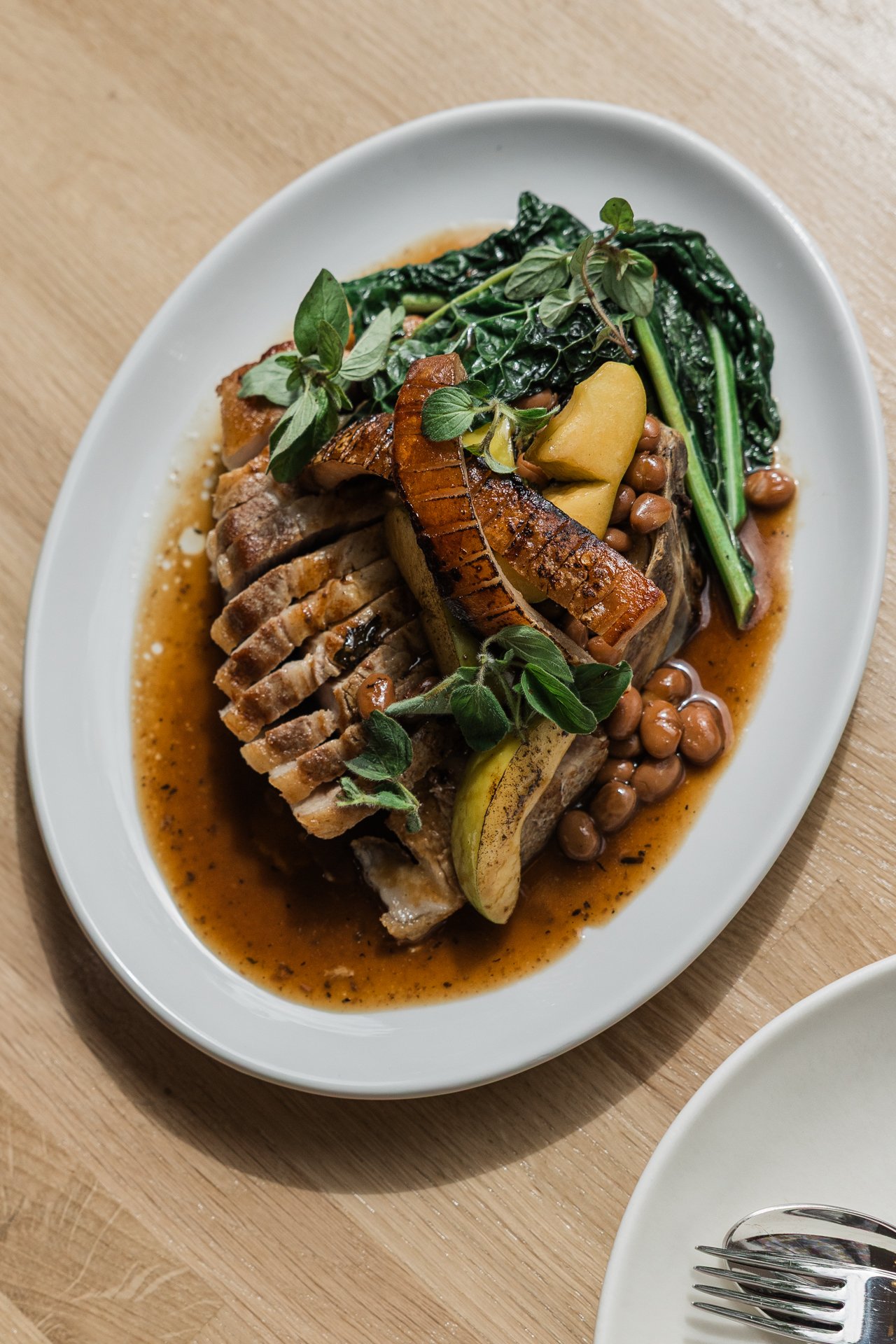 Plate of cooked meat garnished with herbs, vegetables, chickpeas, and sauce.